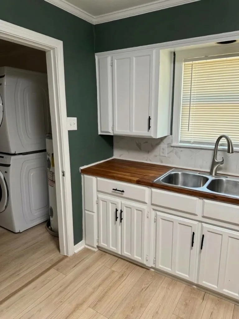 White cabinetry with dark hardware, wood-finish countertops, dual stainless steel sinks, and wood-finish flooring