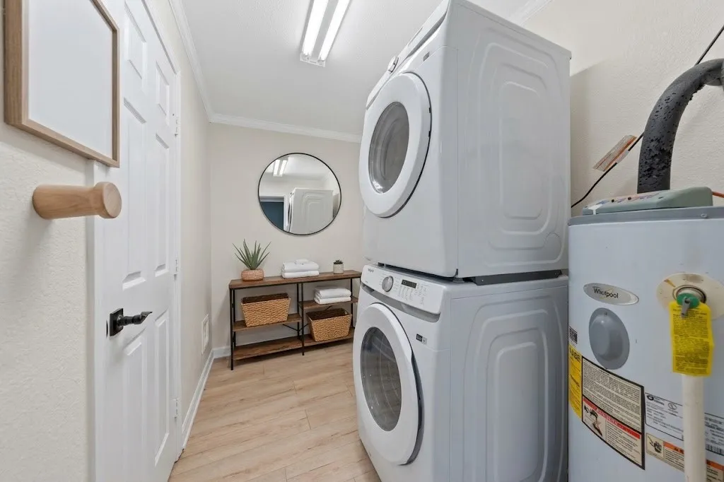 Dedicated laundry area featuring stacked appliances, wood-finish flooring, a wall-mounted mirror, and overhead strip lighting