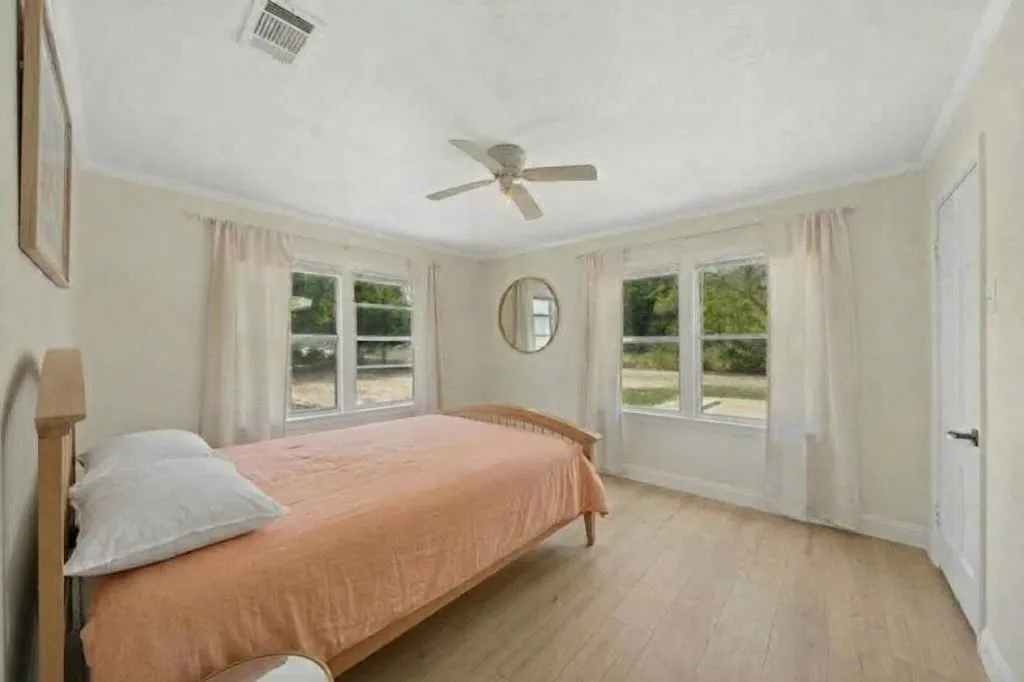 Wood-finish flooring, two large windows, ceiling fan, and white trim throughout