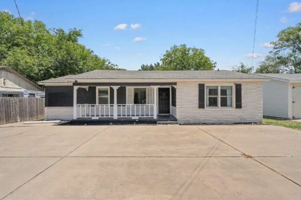 Single-story home featuring a covered front porch with white railing, a white brick facade, and a dark shingled roof