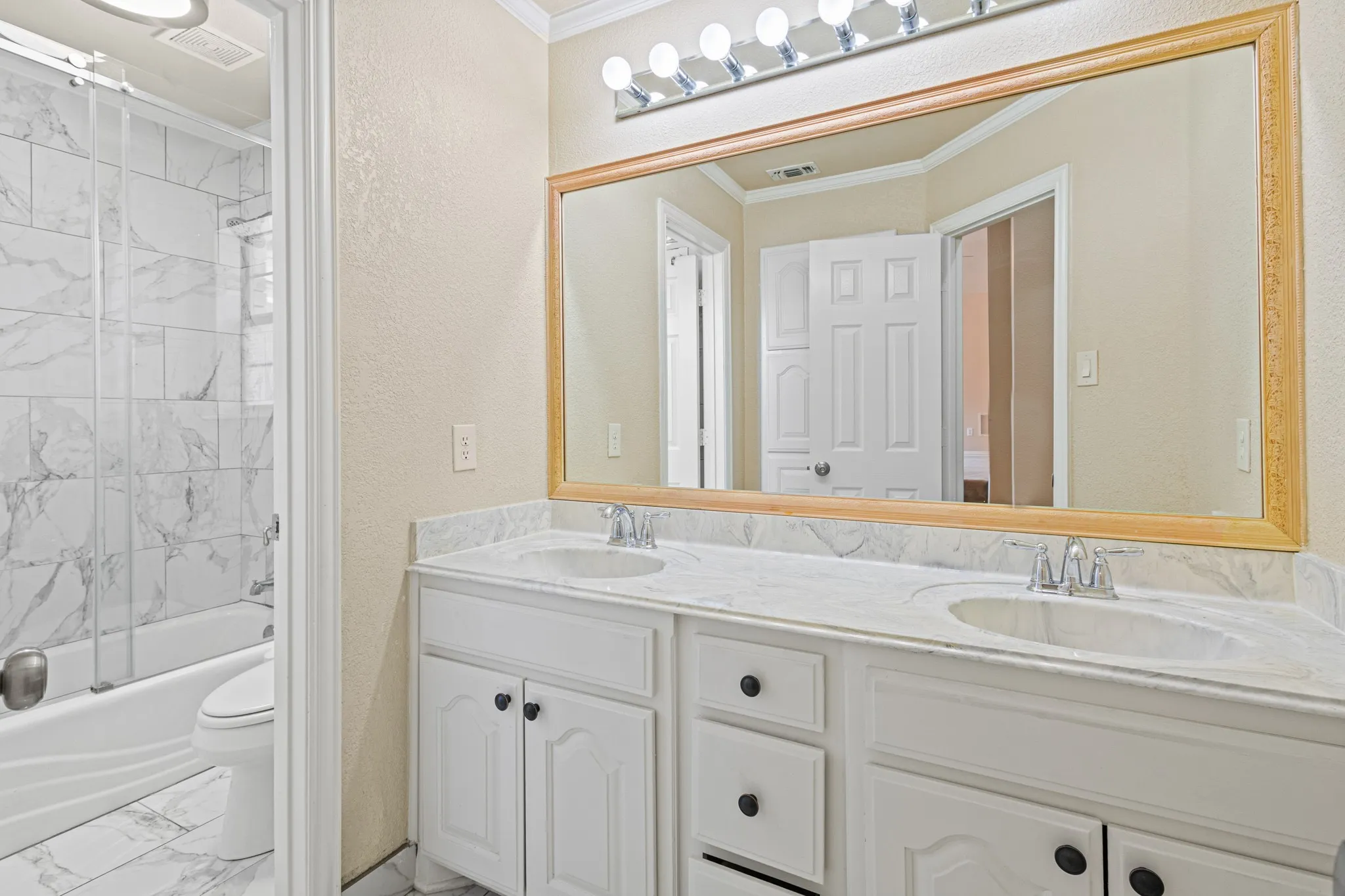 Full bathroom featuring double sink vanity, toilet, tiled shower / bath combo, crown molding, and tile flooring