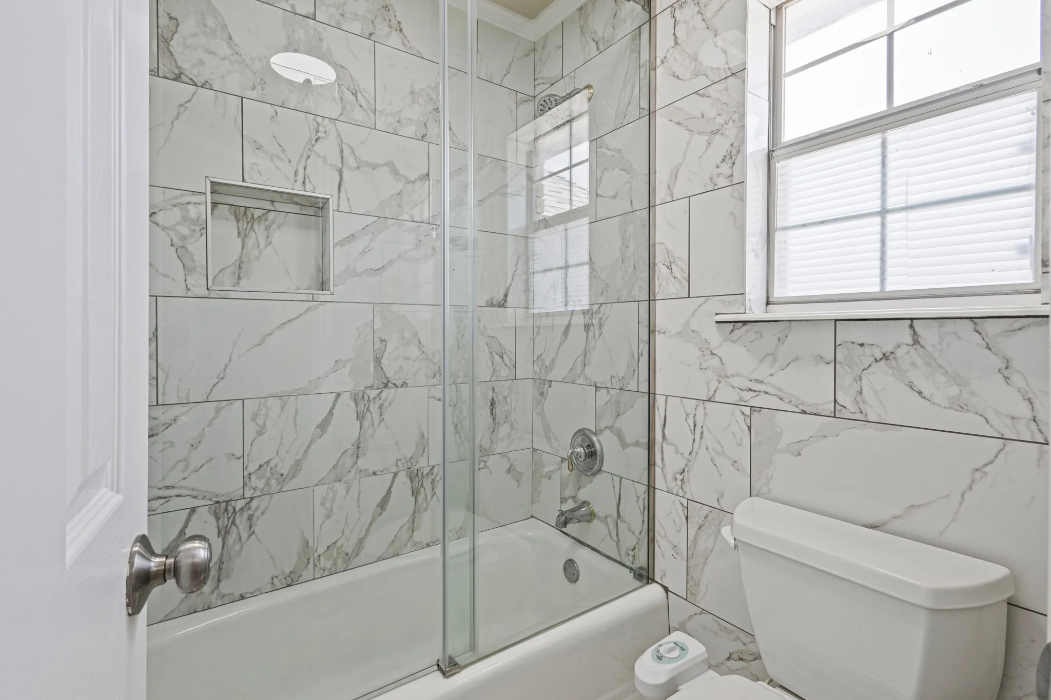 Bathroom featuring combined bath / shower with glass door, toilet, and tile walls