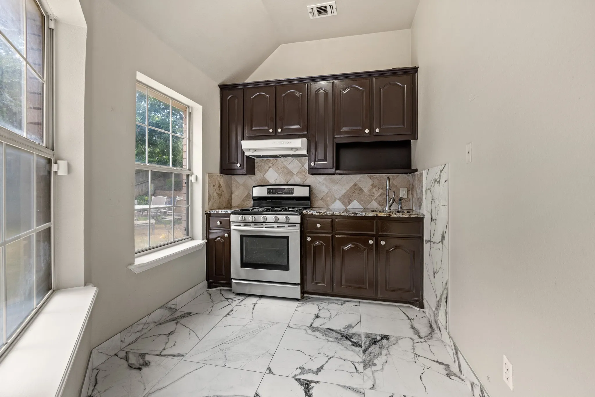 Second full Kitchen with vaulted ceiling, dark brown cabinetry, light tile flooring, backsplash, and gas stove