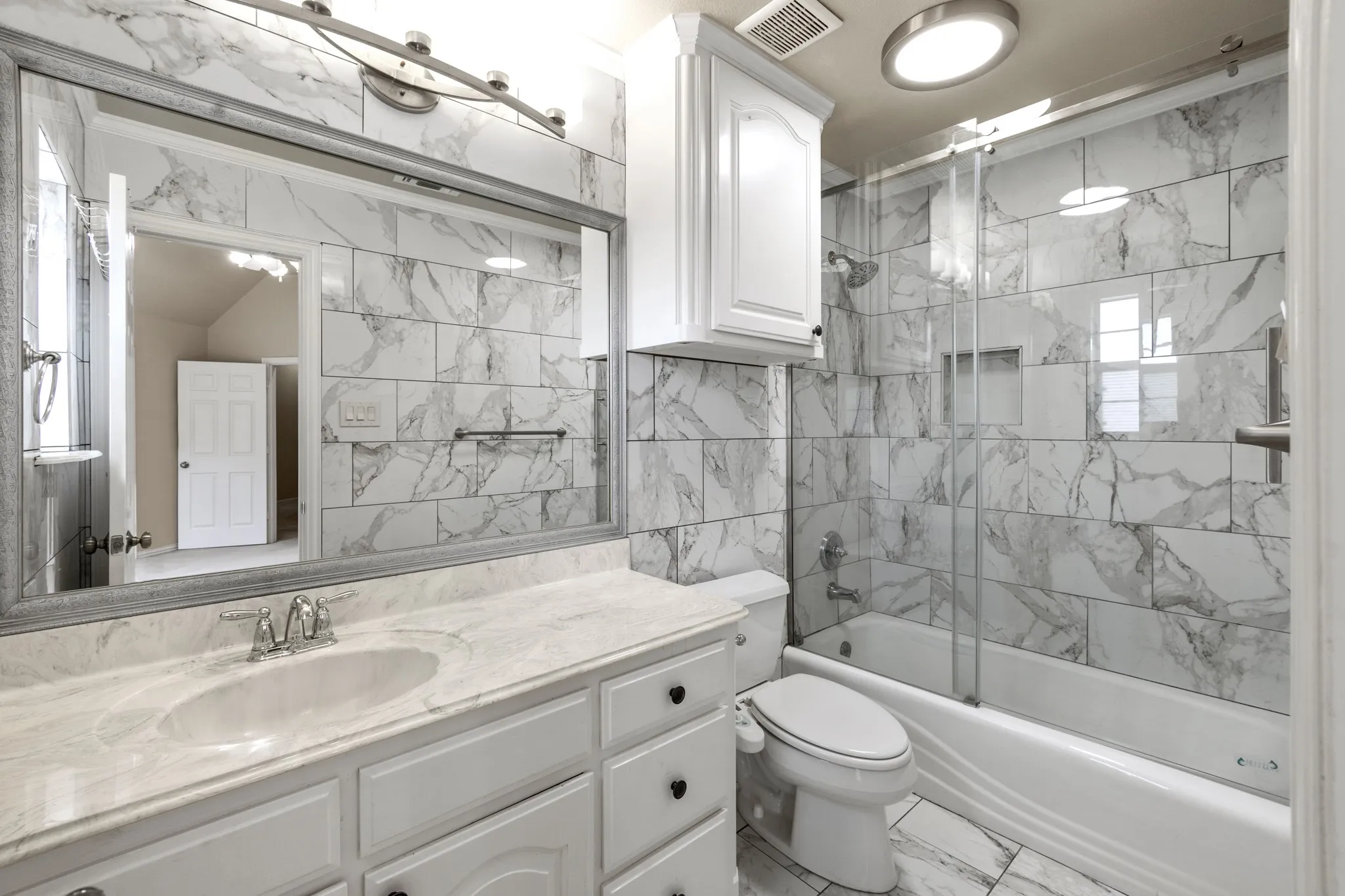 upstairs primary Full bathroom featuring tile floors, bath / shower combo with glass door, tile walls, vanity with extensive cabinet space, and toilet