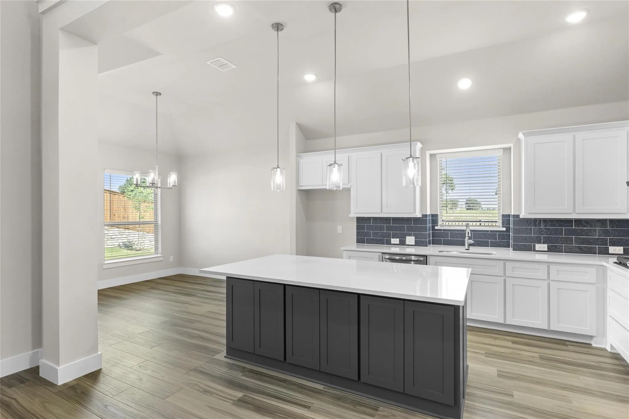 Kitchen featuring a quartz-topped island with dark cabinetry, white perimeter cabinetry, dark subway tile backsplash, and wood-finish flooring