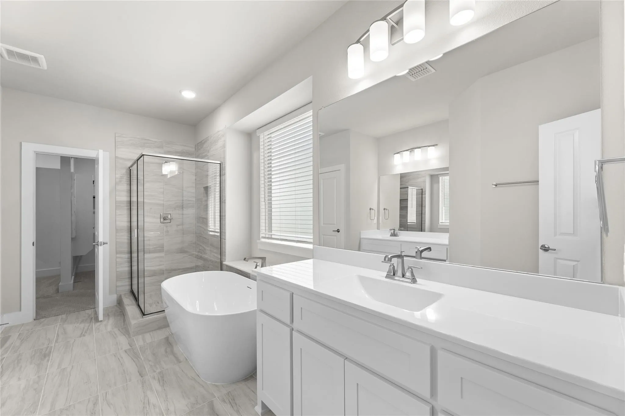 Contemporary bathroom featuring a freestanding soaking tub, a frameless glass shower enclosure with tiled walls, and a dual-sink vanity with white cabinetry and a solid surface countertop