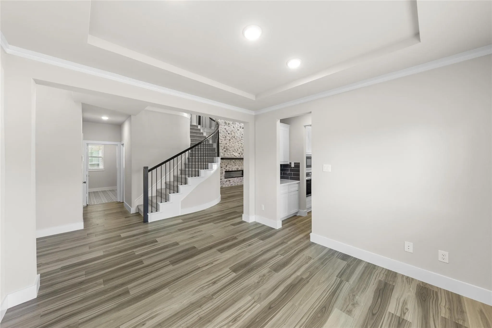 Spacious interior showcasing wood-finish flooring, a contemporary curved staircase with wrought iron balusters, recessed lighting, and tray ceilings