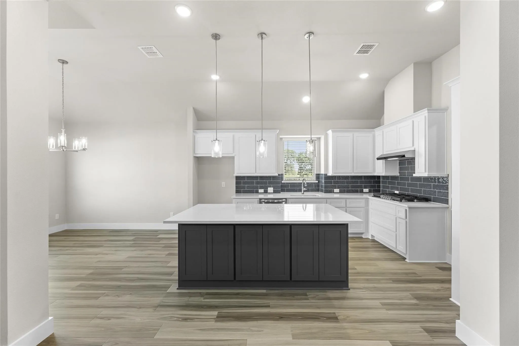 Modern kitchen featuring an island with dark cabinetry and a light-toned countertop, white upper and lower perimeter cabinetry, a dark subway tile backsplash, and stainless steel appliances