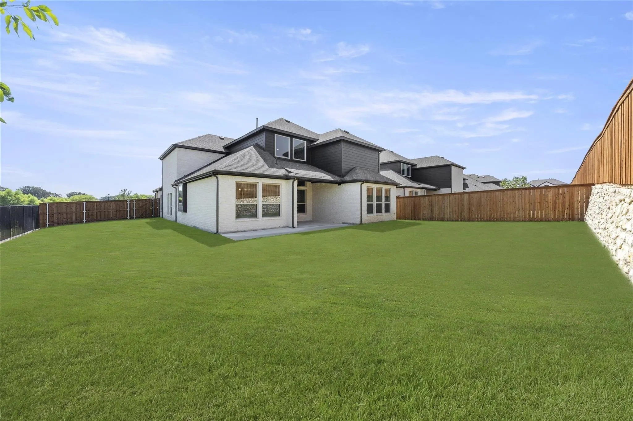 Expansive green lawn with a newly constructed privacy fence, featuring a stone retaining wall
