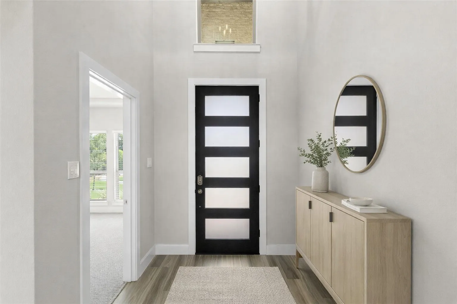 Two-story entryway featuring a modern black front door with frosted glass panels, wood-finish flooring, and a transom window