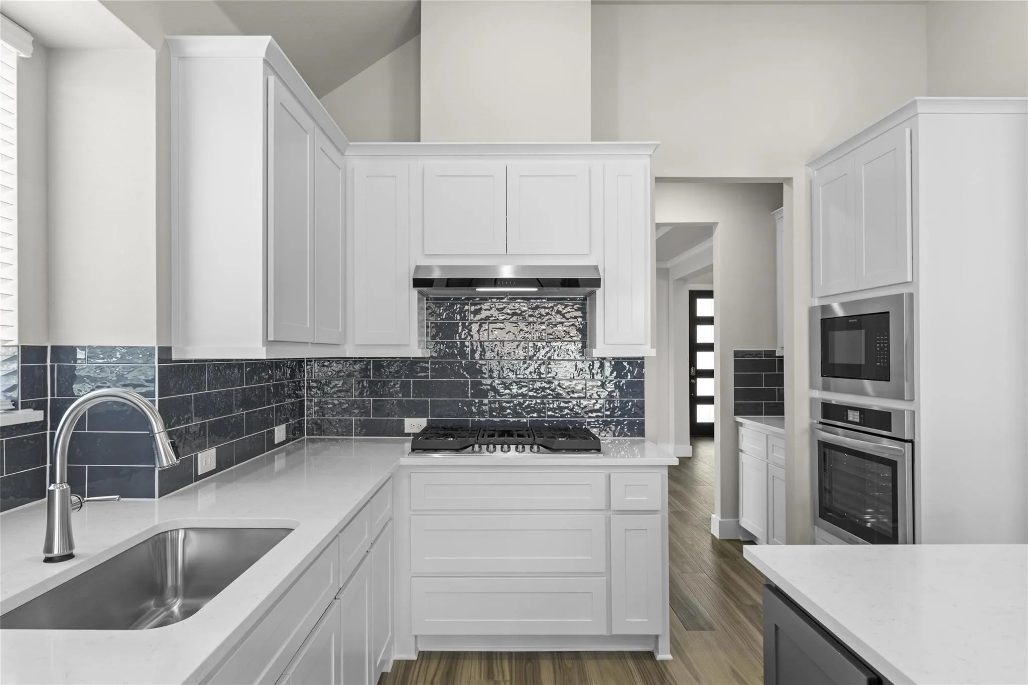 Kitchen featuring white cabinetry, light-toned countertops, dark tile backsplash, stainless steel appliances, and wood-finish flooring