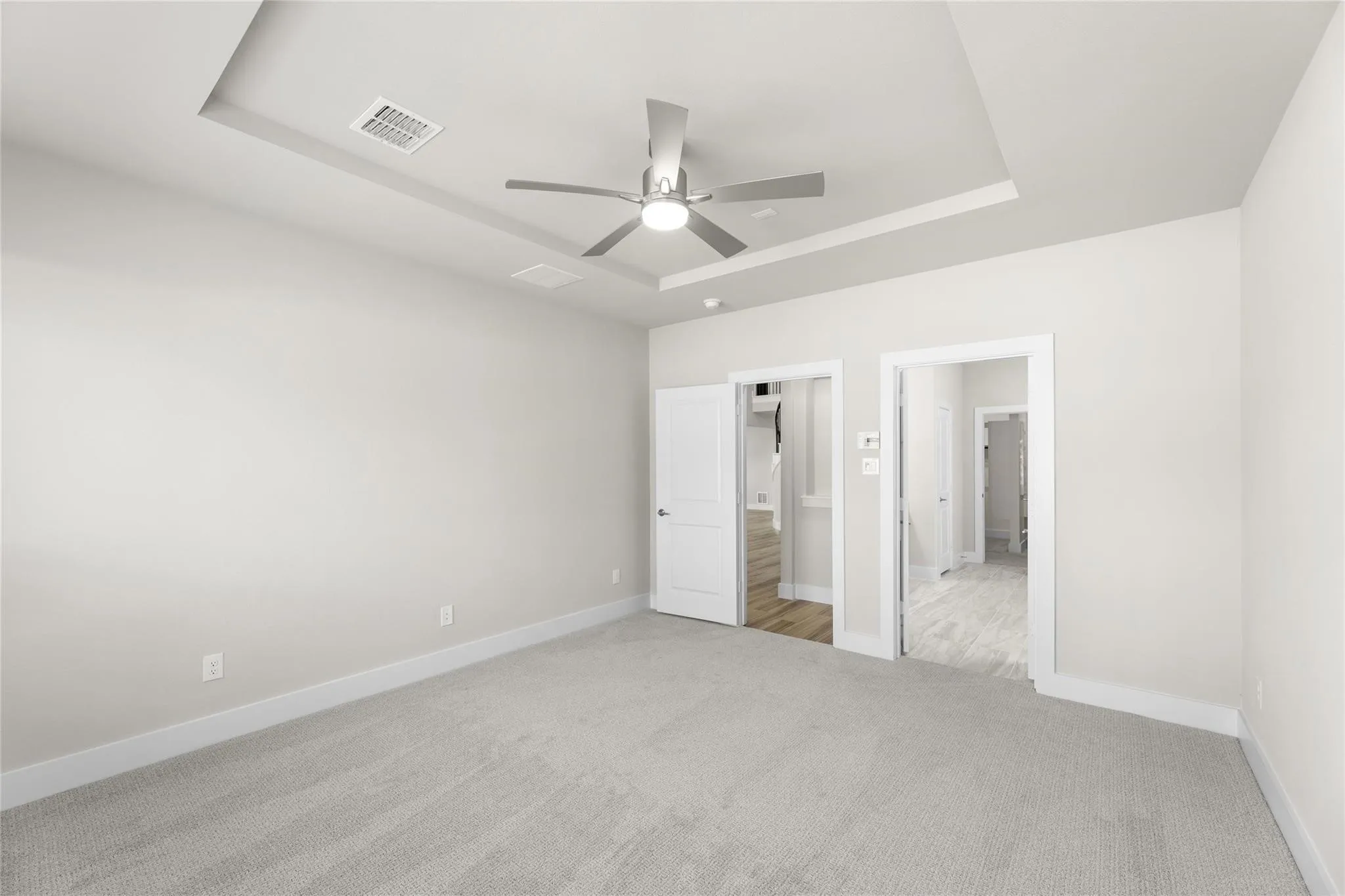 Spacious room with light gray carpeting, tray ceiling, and a modern ceiling fan with integrated lighting