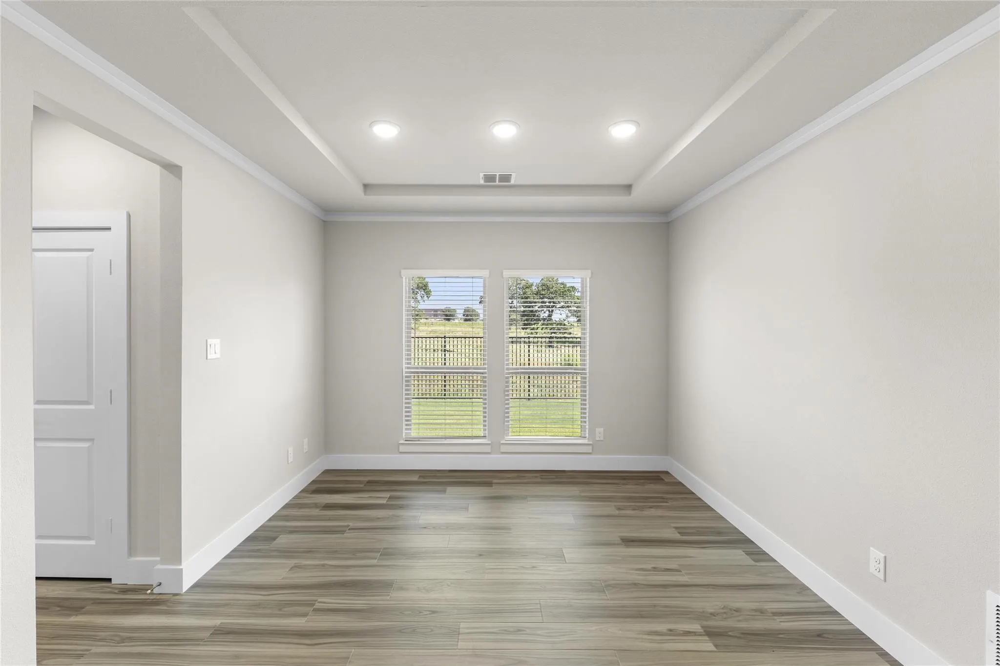 Interior room with wood-finish flooring, light-toned walls, and a tray ceiling with recessed lighting