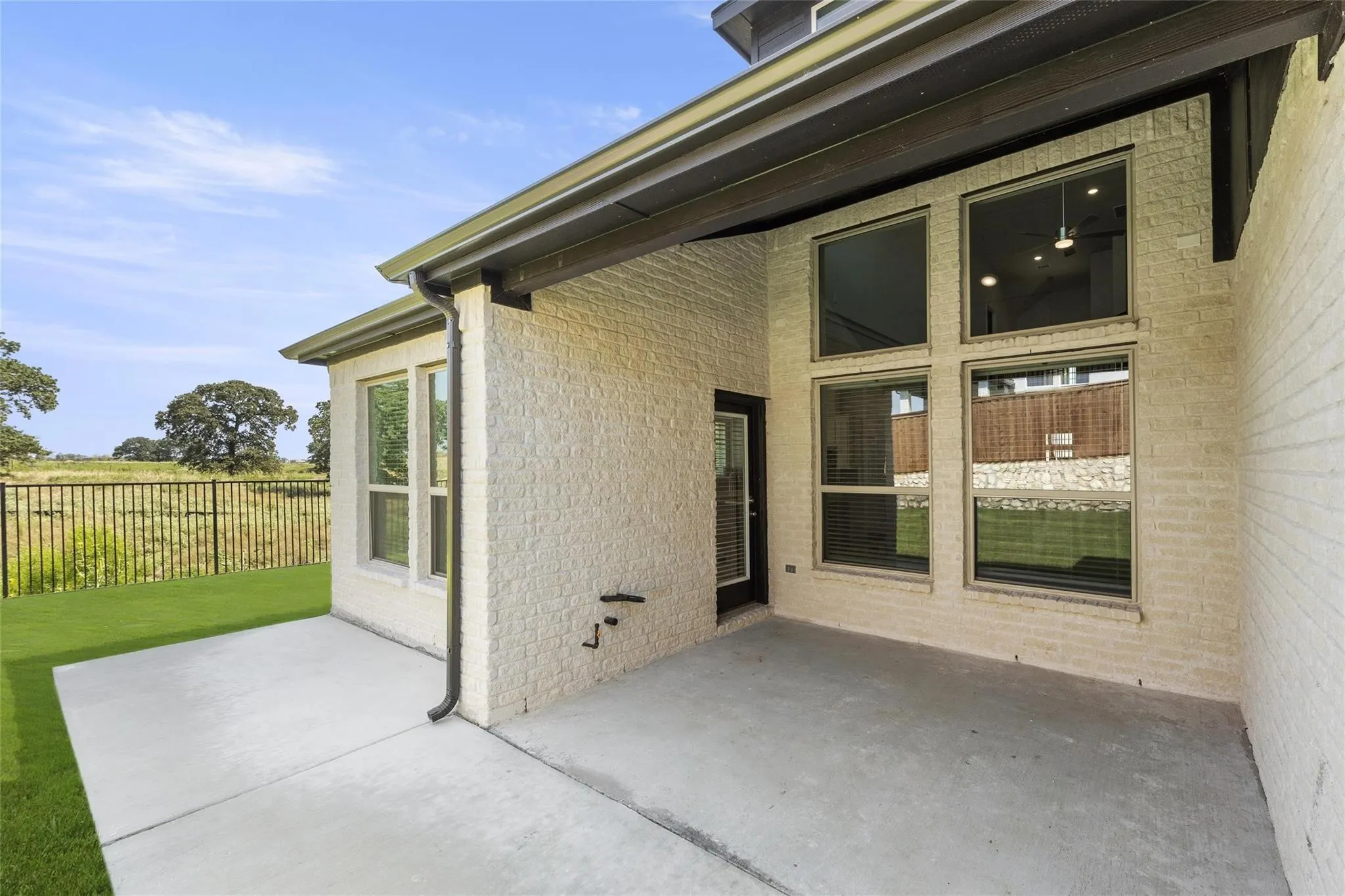 Expansive covered patio featuring a concrete surface, white brick exterior, and a series of large windows