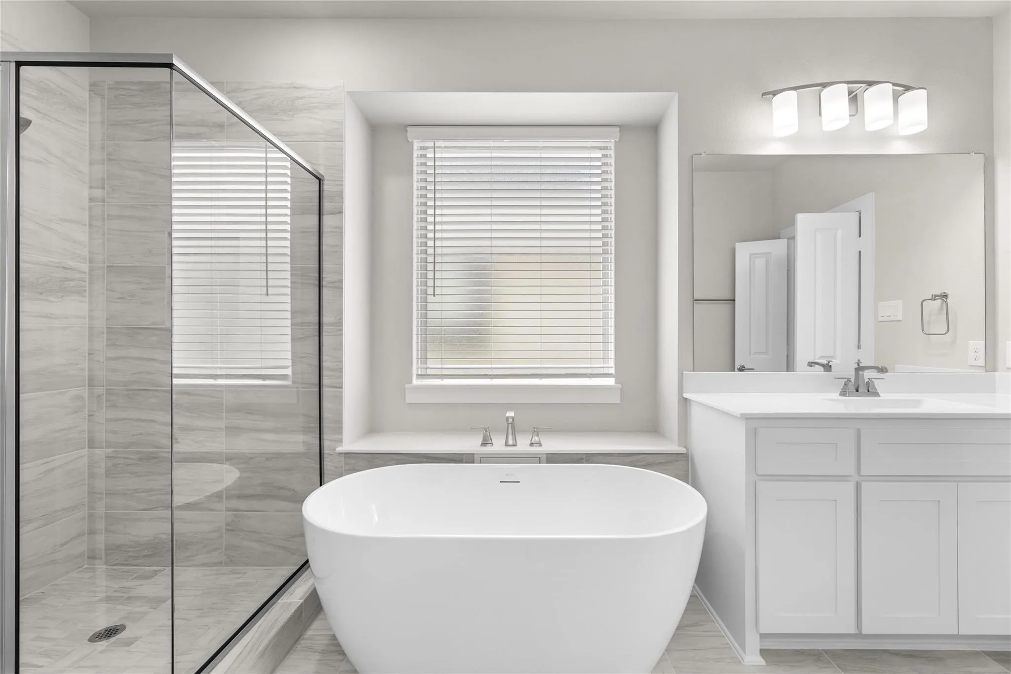 Freestanding soaking tub, glass-enclosed shower with tiled surround, dual vanity with white cabinetry, and contemporary lighting fixture