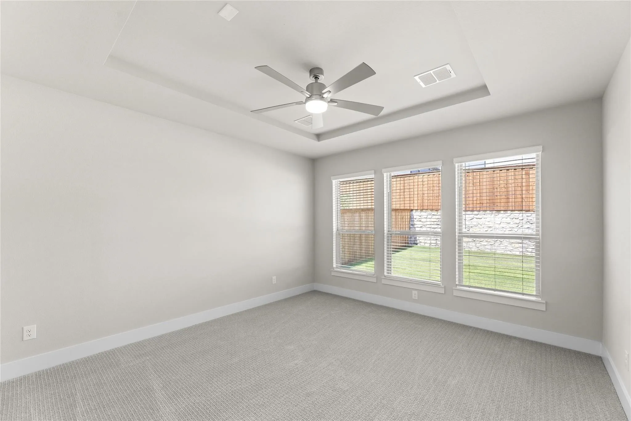 Spacious room featuring light-toned carpeting, a tray ceiling with a modern ceiling fan, and three large windows
