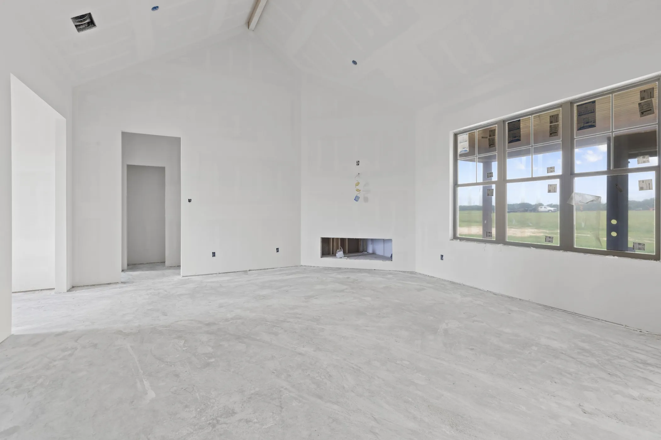 Spacious interior showcasing a vaulted ceiling, large multi-pane windows, and a recessed fireplace opening