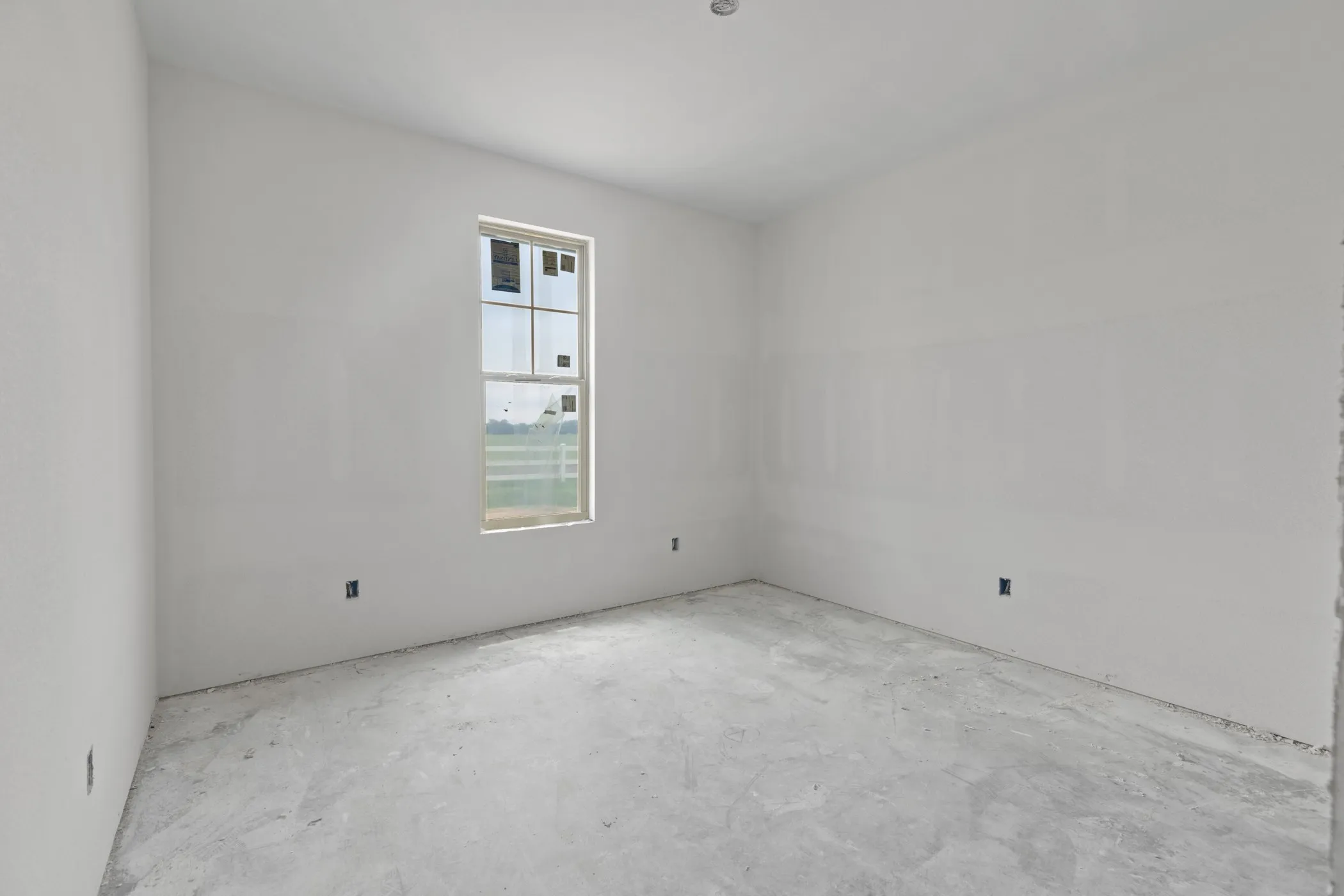 Room with a window, white walls, and concrete flooring