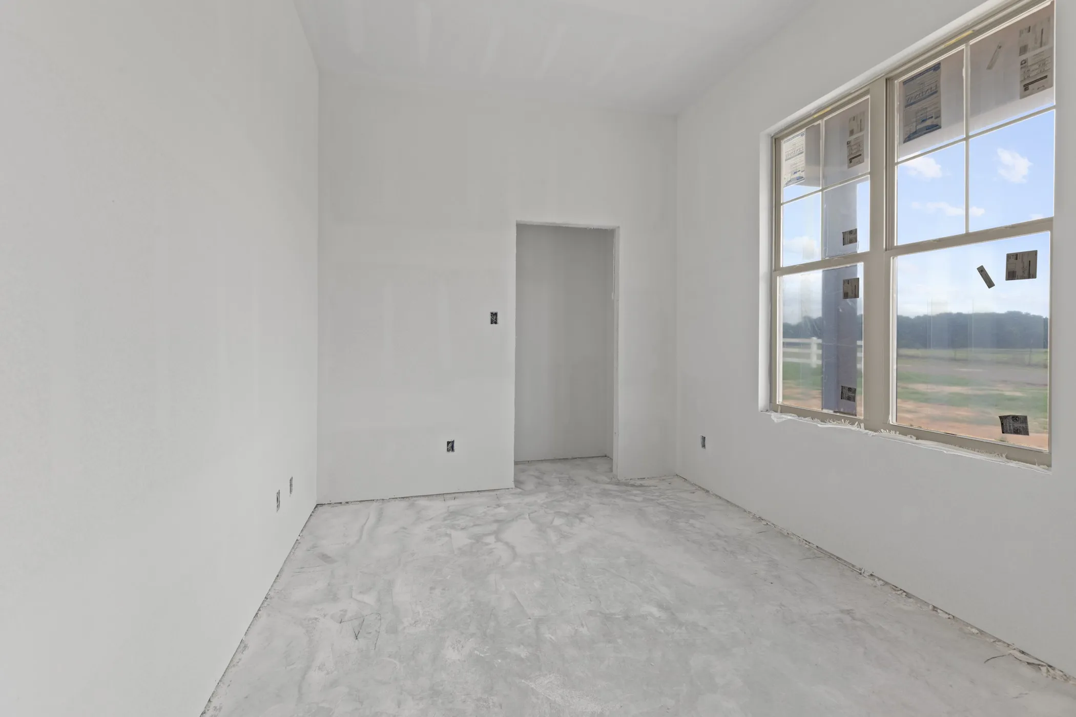 Spacious room featuring a large multi-pane window, an open doorway, neutral wall finishes, and a raw concrete floor