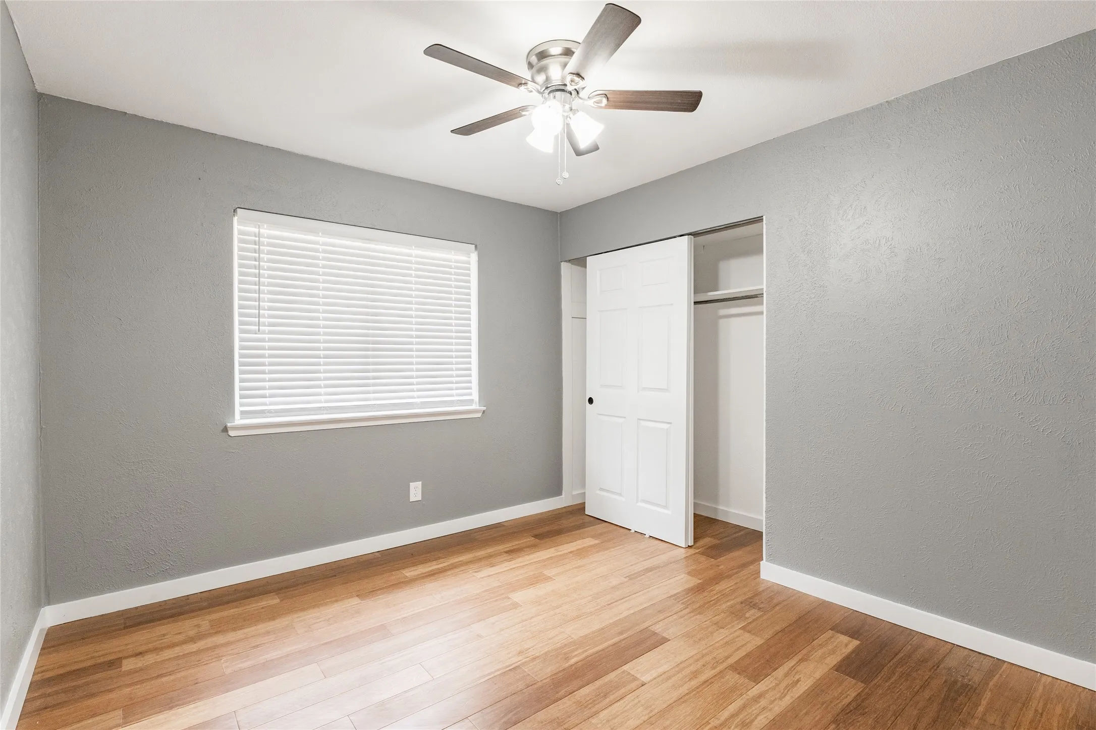 Spacious room with wood-finish flooring, light grey walls, and white baseboards