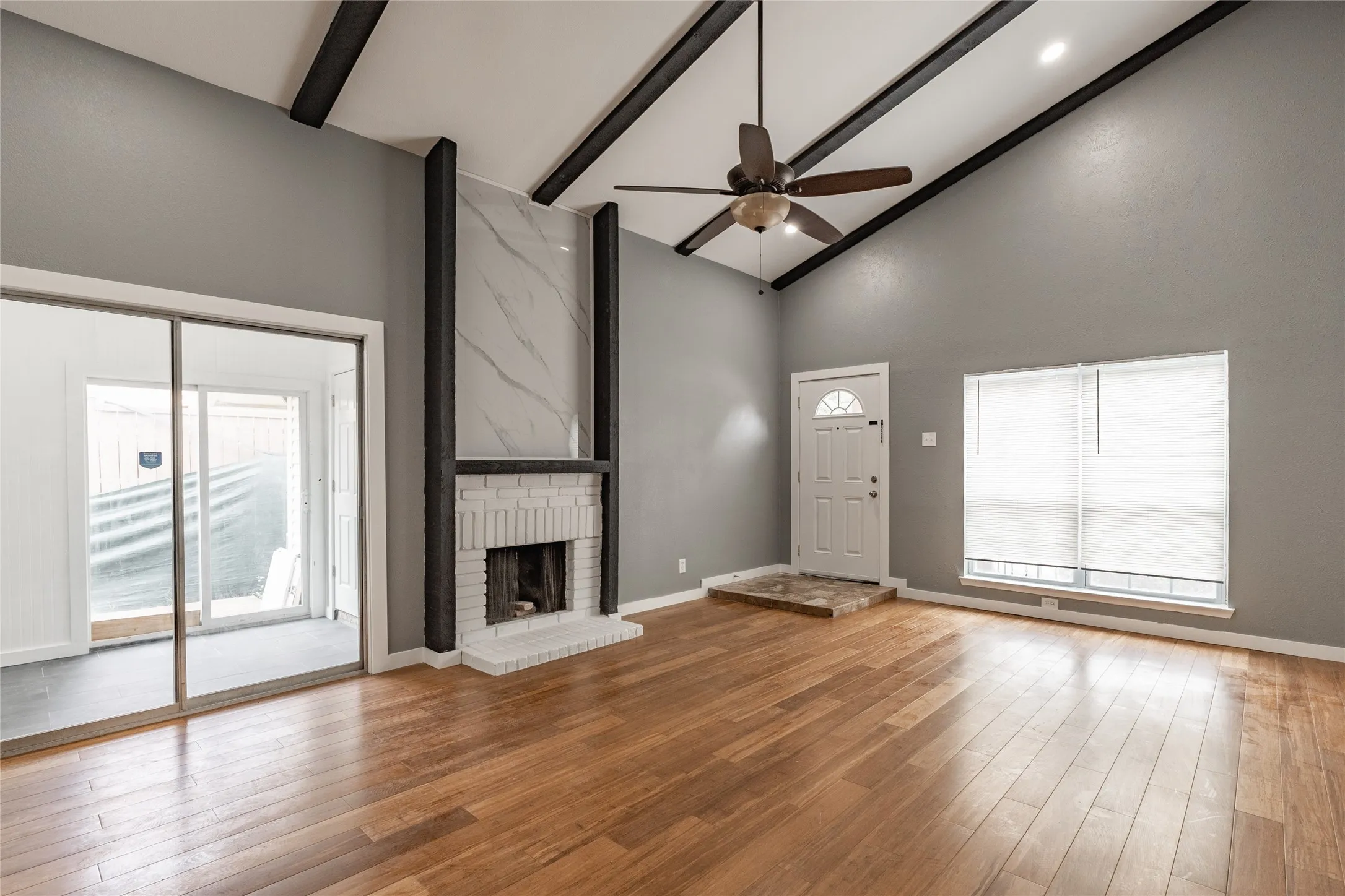 Vaulted ceiling living area featuring wood-finish flooring, a white brick fireplace with a stone surround, and sliding glass doors