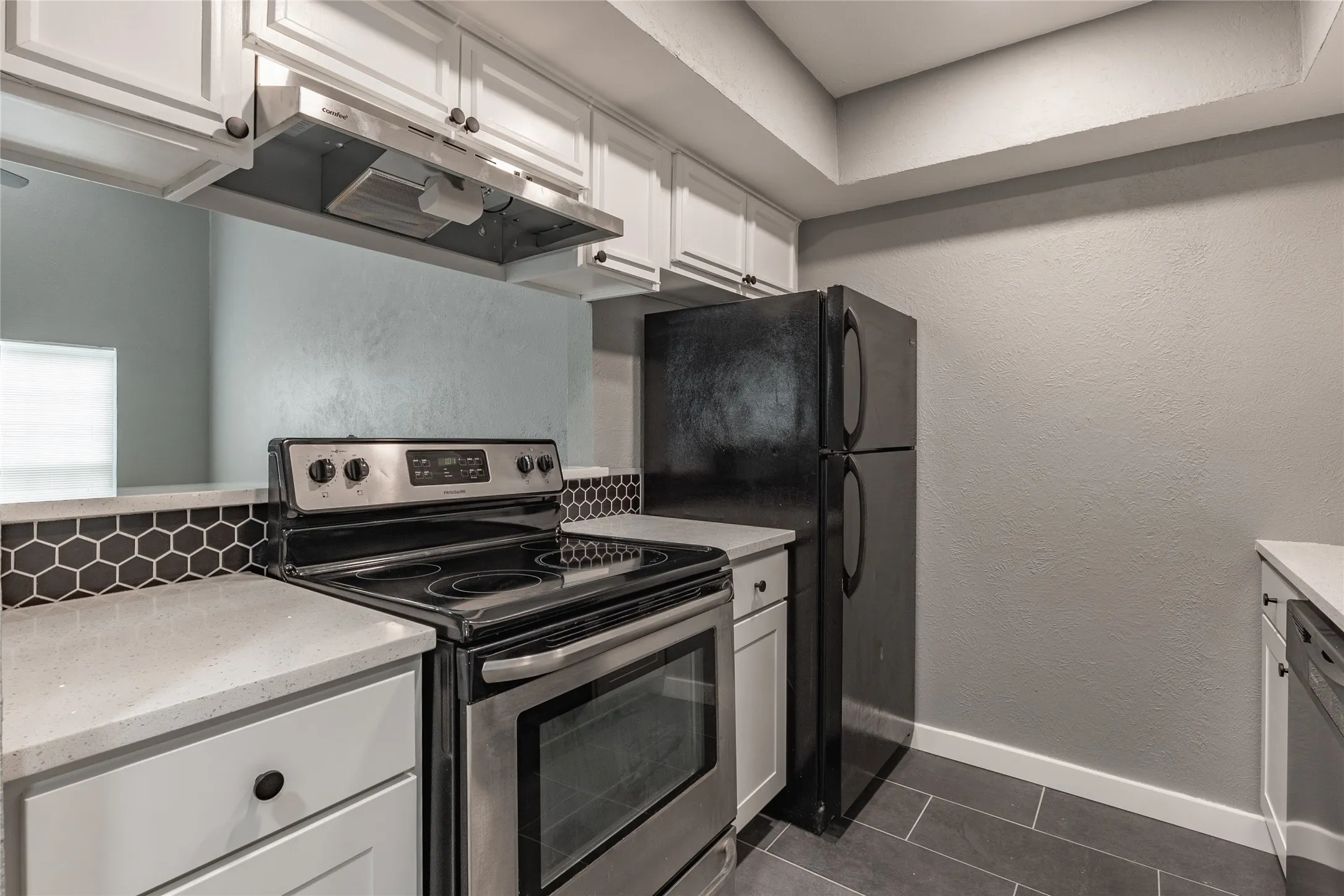 Modern kitchen featuring white shaker cabinetry, light-toned countertops, a stainless steel electric range, and a black hexagon tile backsplash
