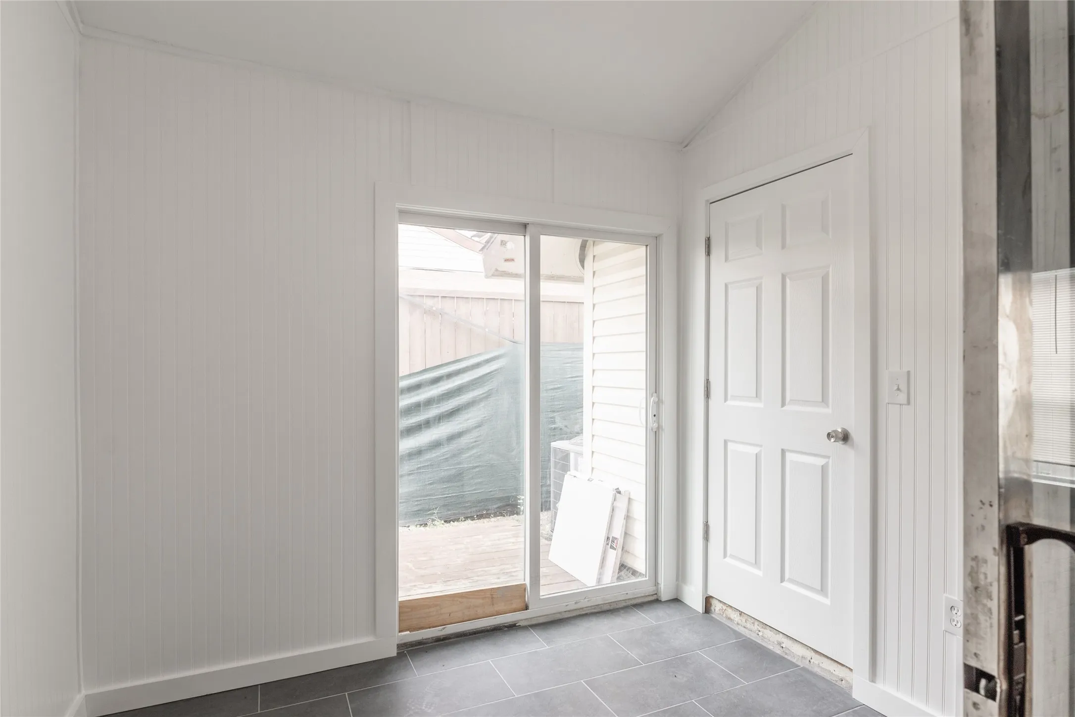 Interior space featuring beadboard wall paneling, dark tile flooring, a sliding glass door providing exterior access, and a six-panel door