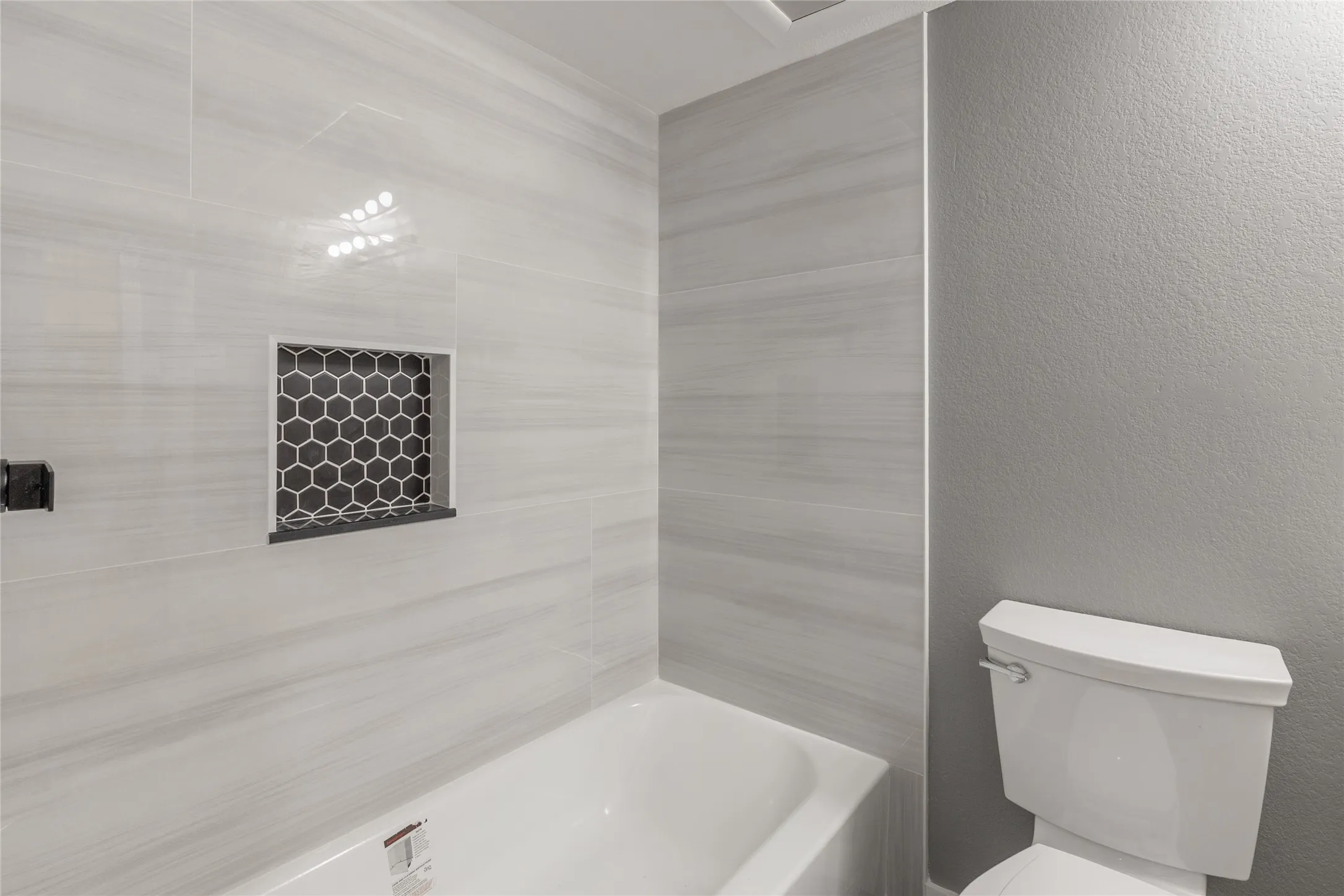 Bathtub and shower surround featuring large format tile with subtle veining
