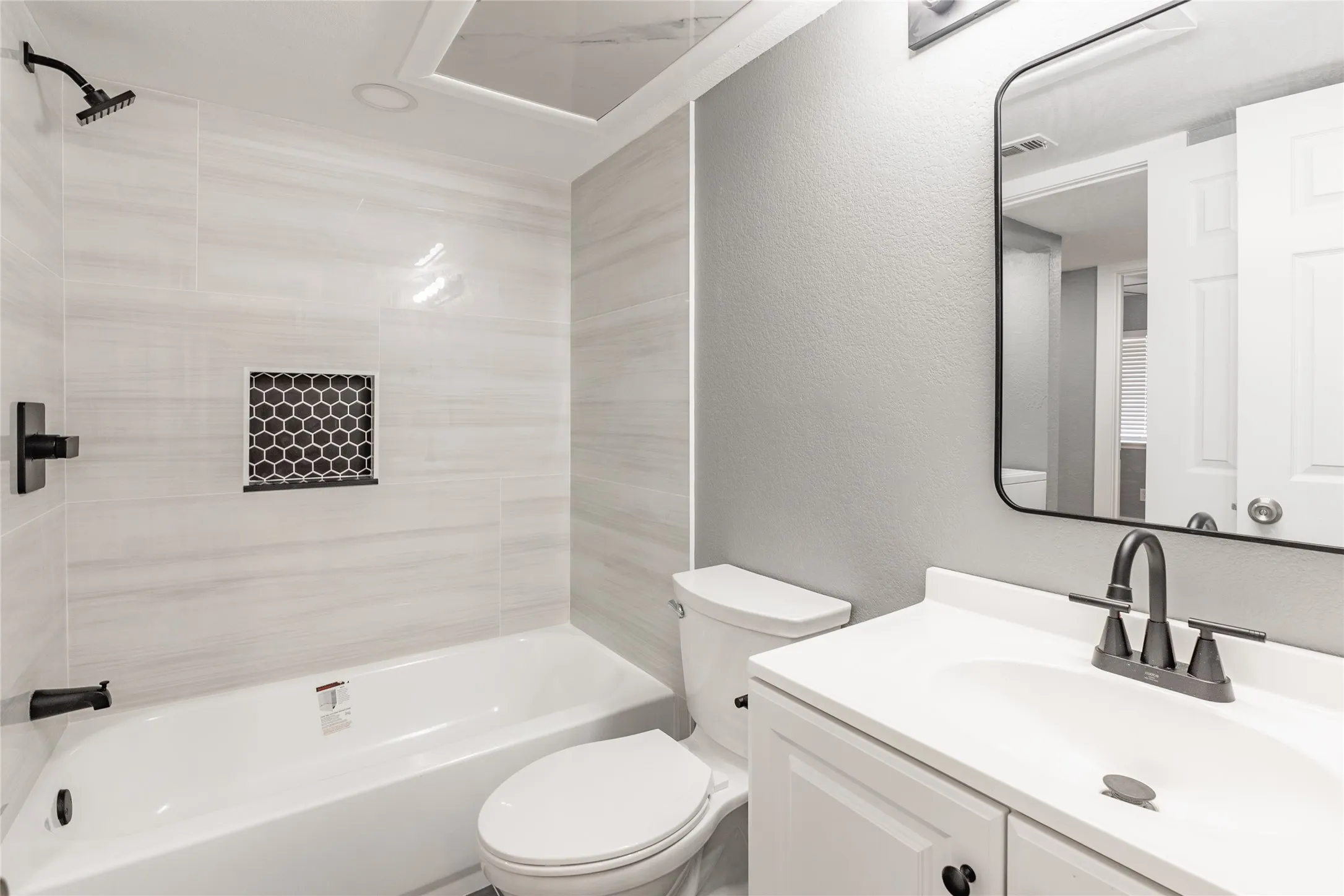 Bathroom featuring a white bathtub, light-toned wall tiling, black fixtures, and an integrated shower niche with mosaic tile