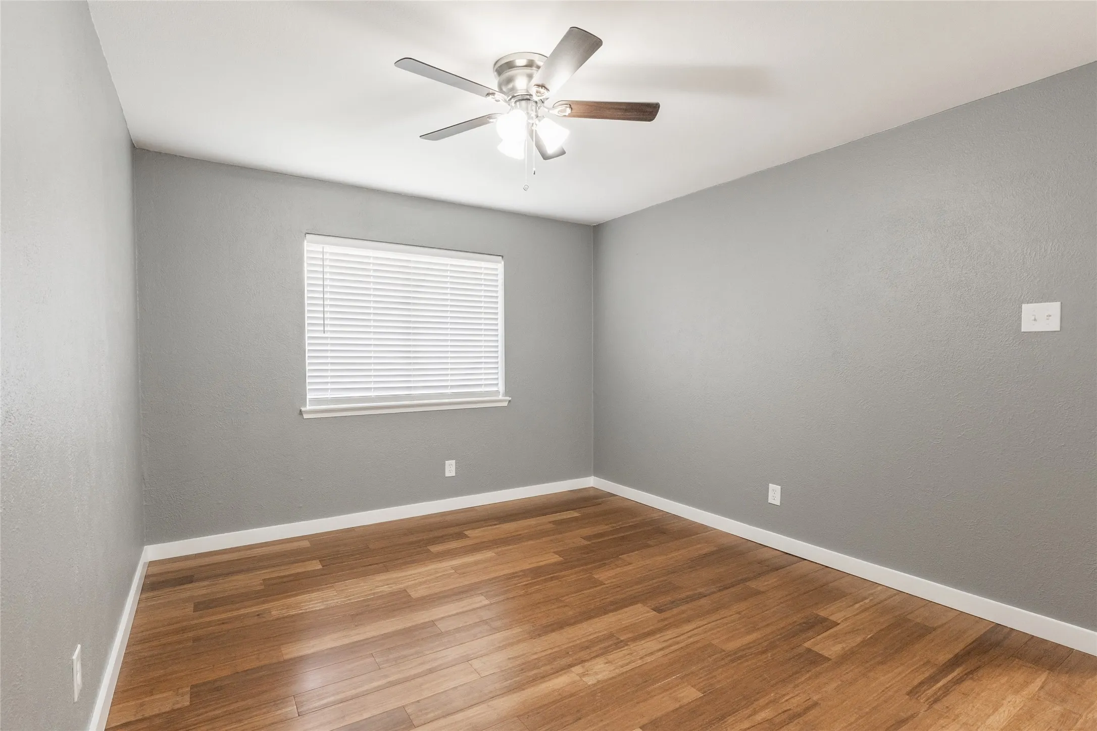 Room featuring wood-finish flooring, light gray walls, white trim, and a ceiling fan with integrated lighting