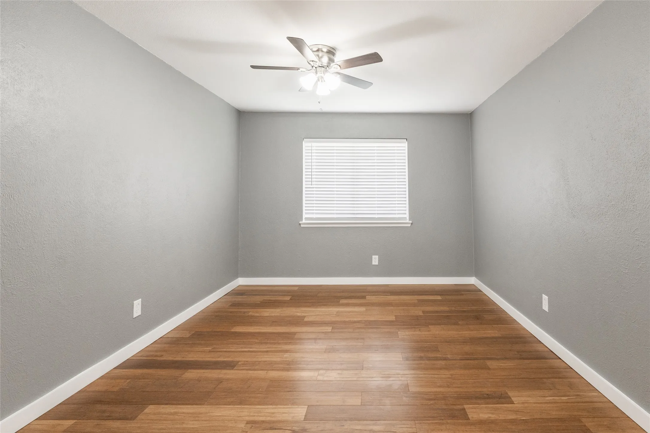Room featuring wood-finish flooring, light gray walls, white trim, and a ceiling fan with integrated lighting