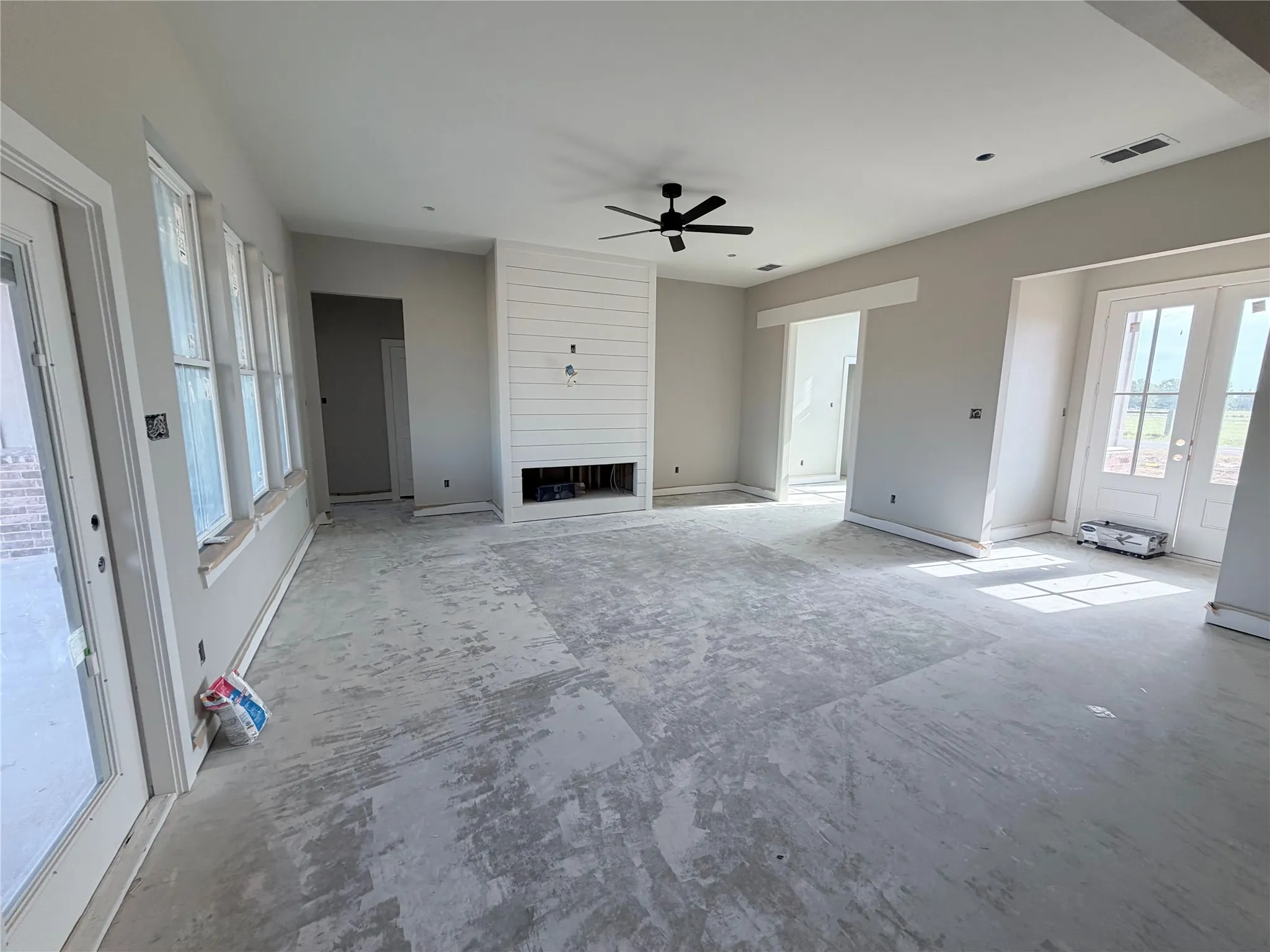 Shiplap accent wall, built-in fireplace, ceiling fan, multiple windows, and double patio doors