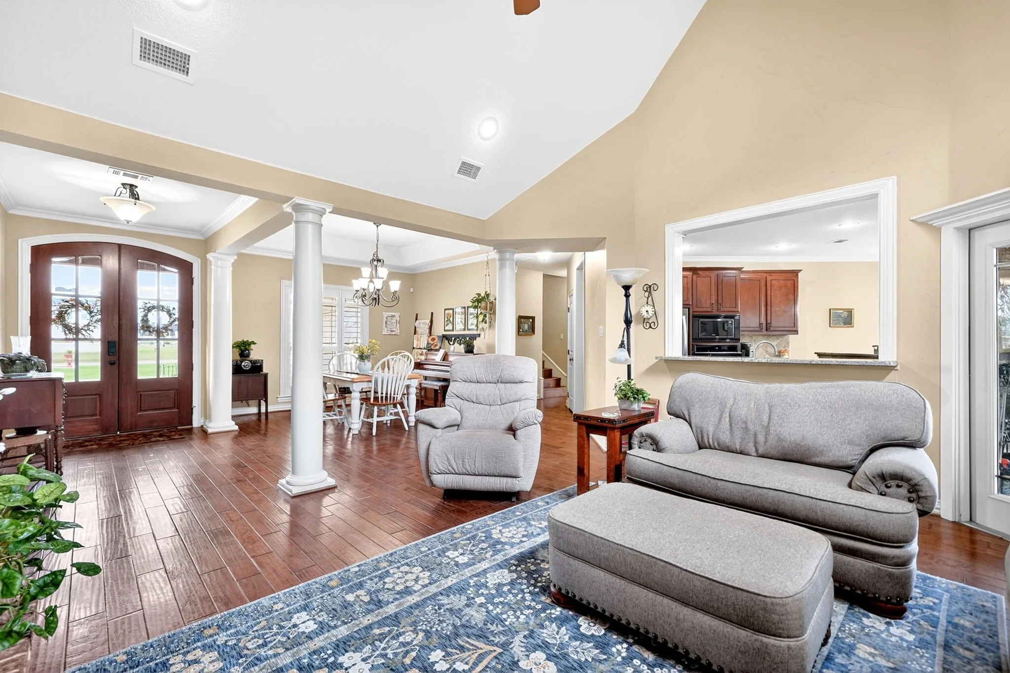 Expansive living area featuring vaulted ceilings, wood-finish flooring, and architectural columns