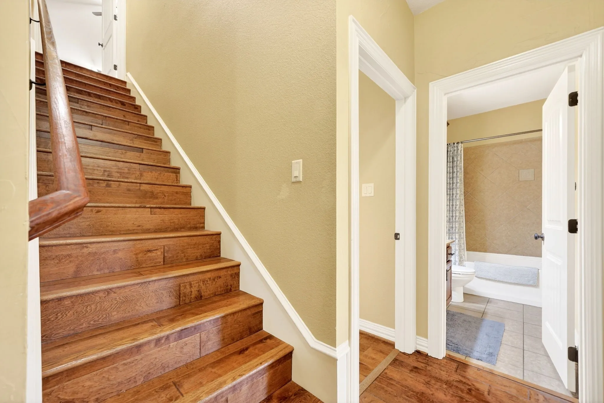 Wood-finish flooring throughout the hallway and staircase, featuring a carved wood handrail
