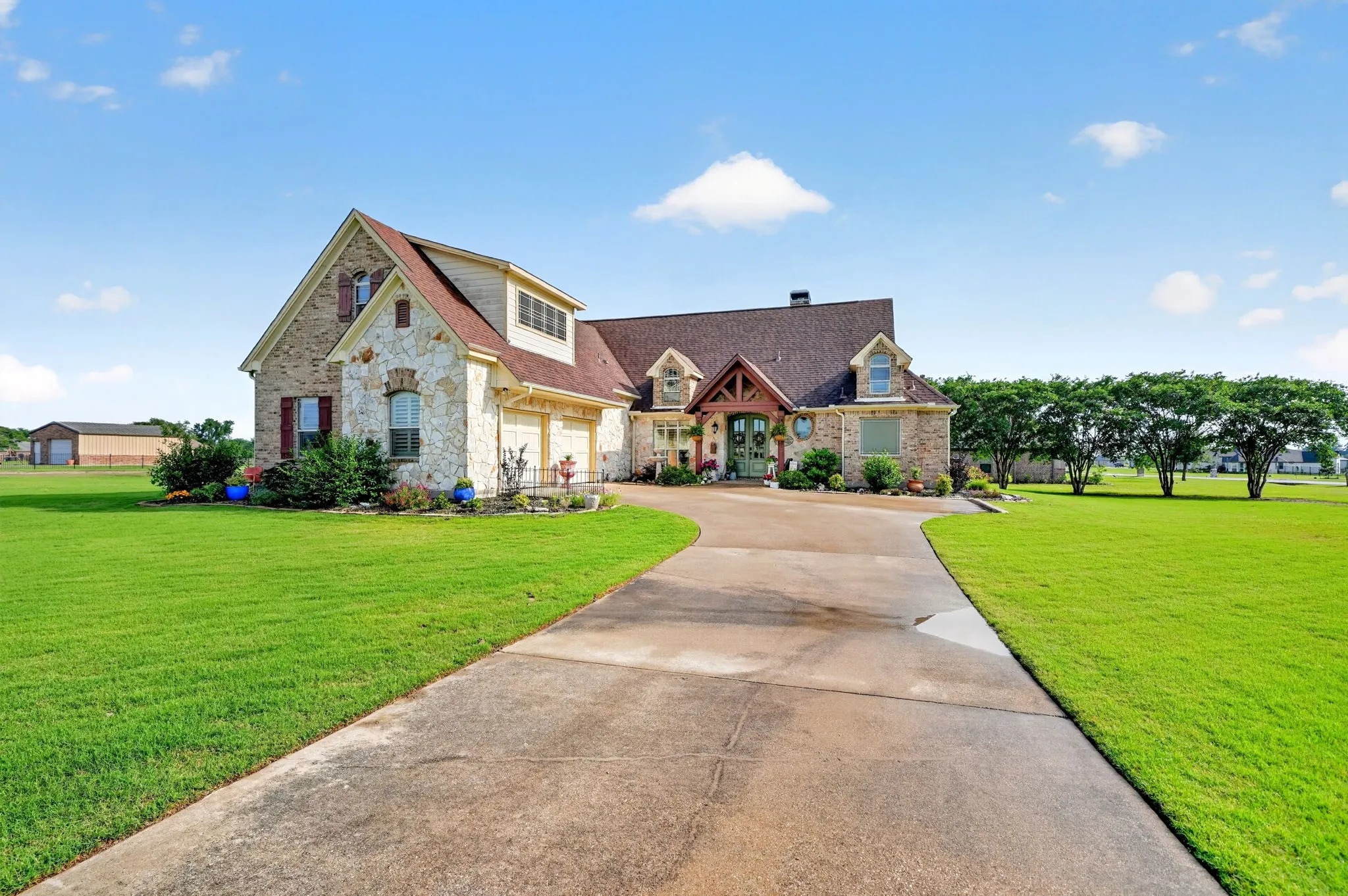 Expansive residential property featuring a stone and brick exterior, a multi-gabled roofline, a curved concrete driveway, and a verdant lawn
