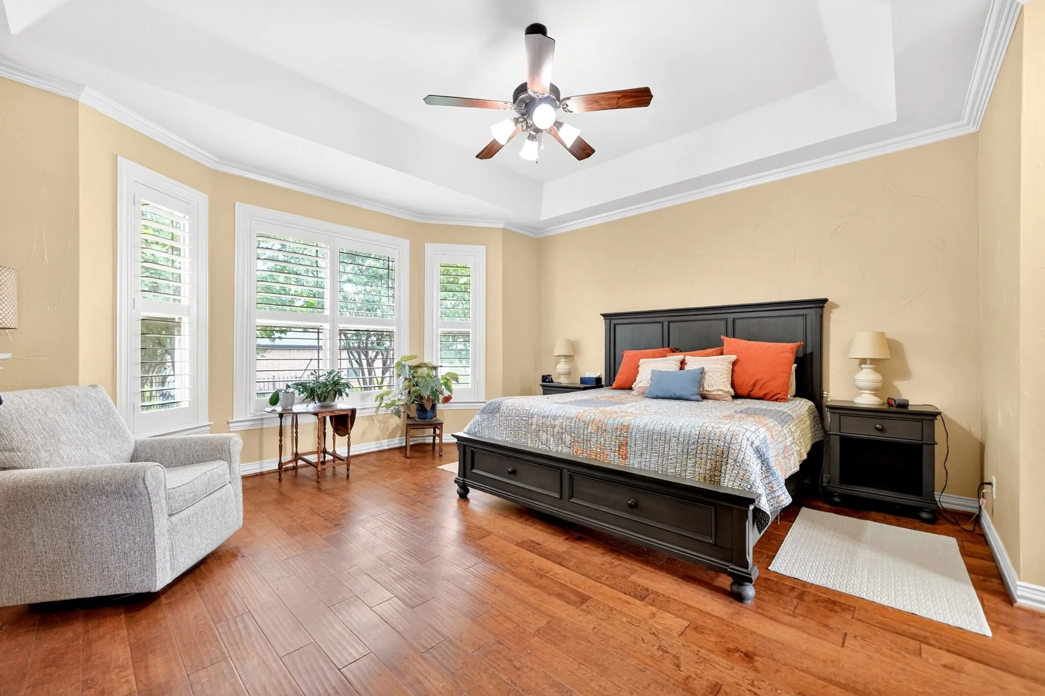 Spacious room with rich wood-finish flooring, a tray ceiling, and a ceiling fan with integrated lighting
