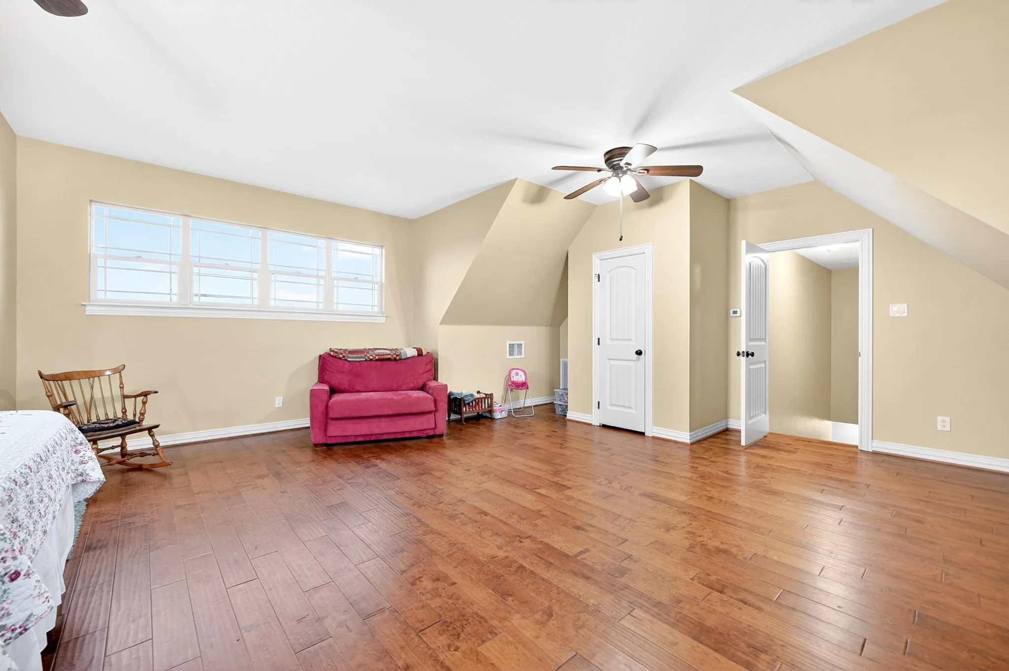 Spacious room featuring wood-finish flooring, multiple windows, a ceiling fan, and architectural sloped ceilings