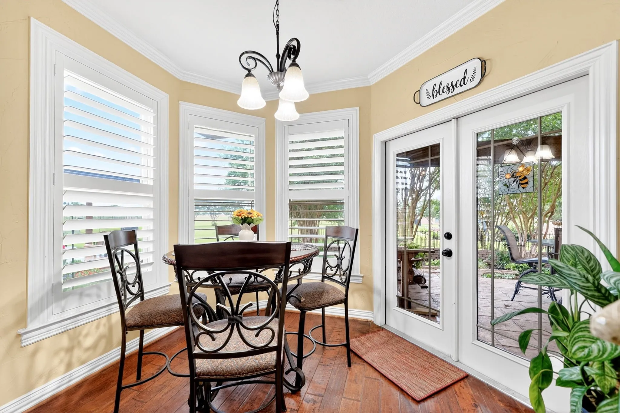 Dining area featuring wood-finish flooring, white plantation shutters, a multi-light pendant fixture, and French doors opening to an outdoor patio with a paved surface