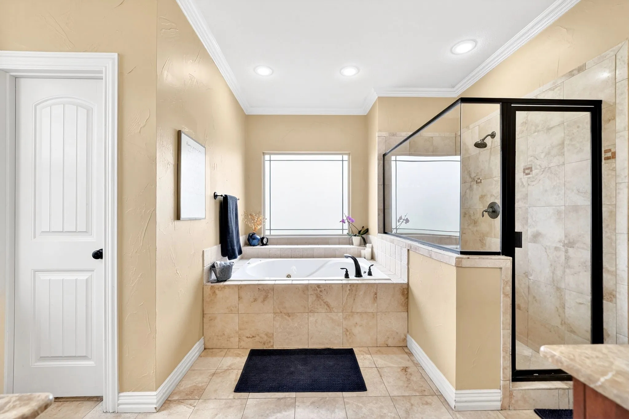 Spacious bathroom featuring a built-in soaking tub with a tiled surround, a separate glass-enclosed shower with tiled walls, recessed lighting, crown molding, and tiled flooring