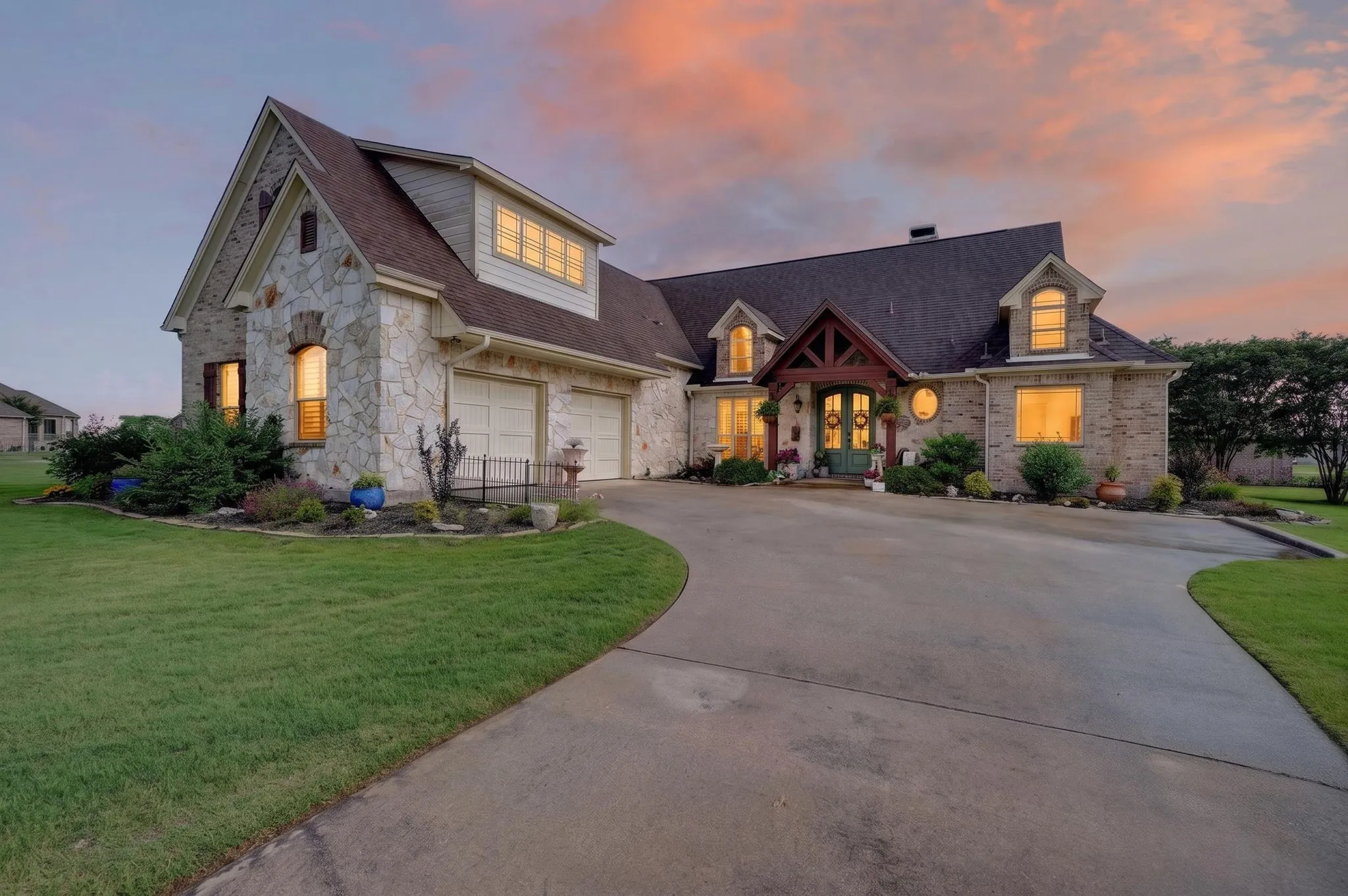 Stone and brick exterior residence featuring a curved driveway, an attached two-car garage, dormer windows, and a covered entry with exposed timber framing