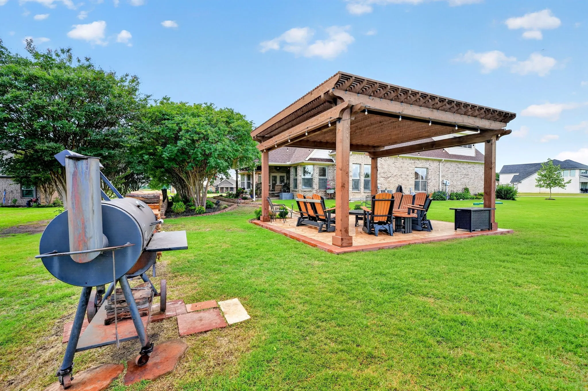 Expansive backyard featuring a custom wooden pergola over a stamped concrete patio, string lighting, and mature perimeter trees