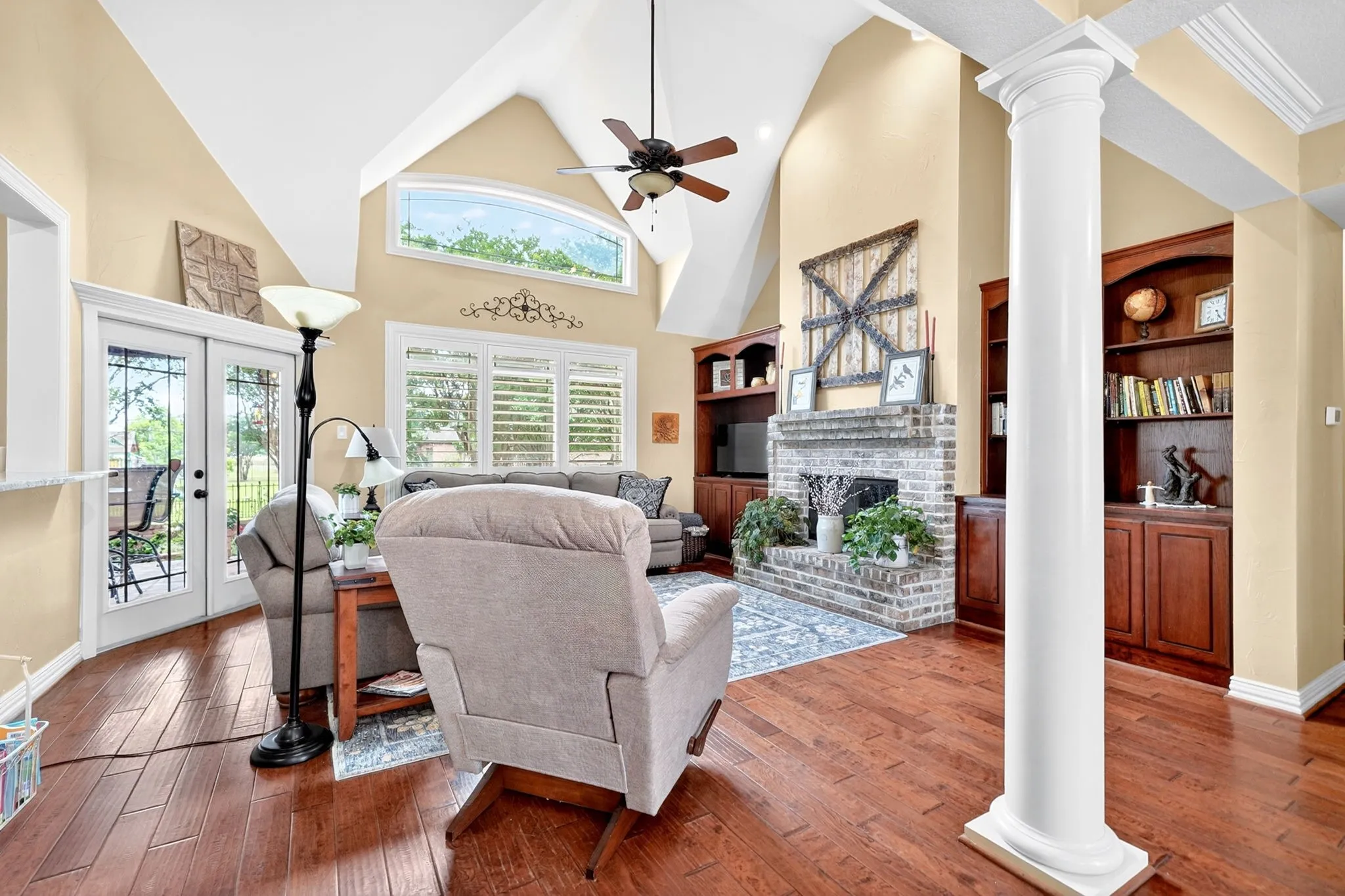 Spacious living area featuring vaulted ceilings with exposed beams, wood-finish flooring, and a brick fireplace with built-in shelving