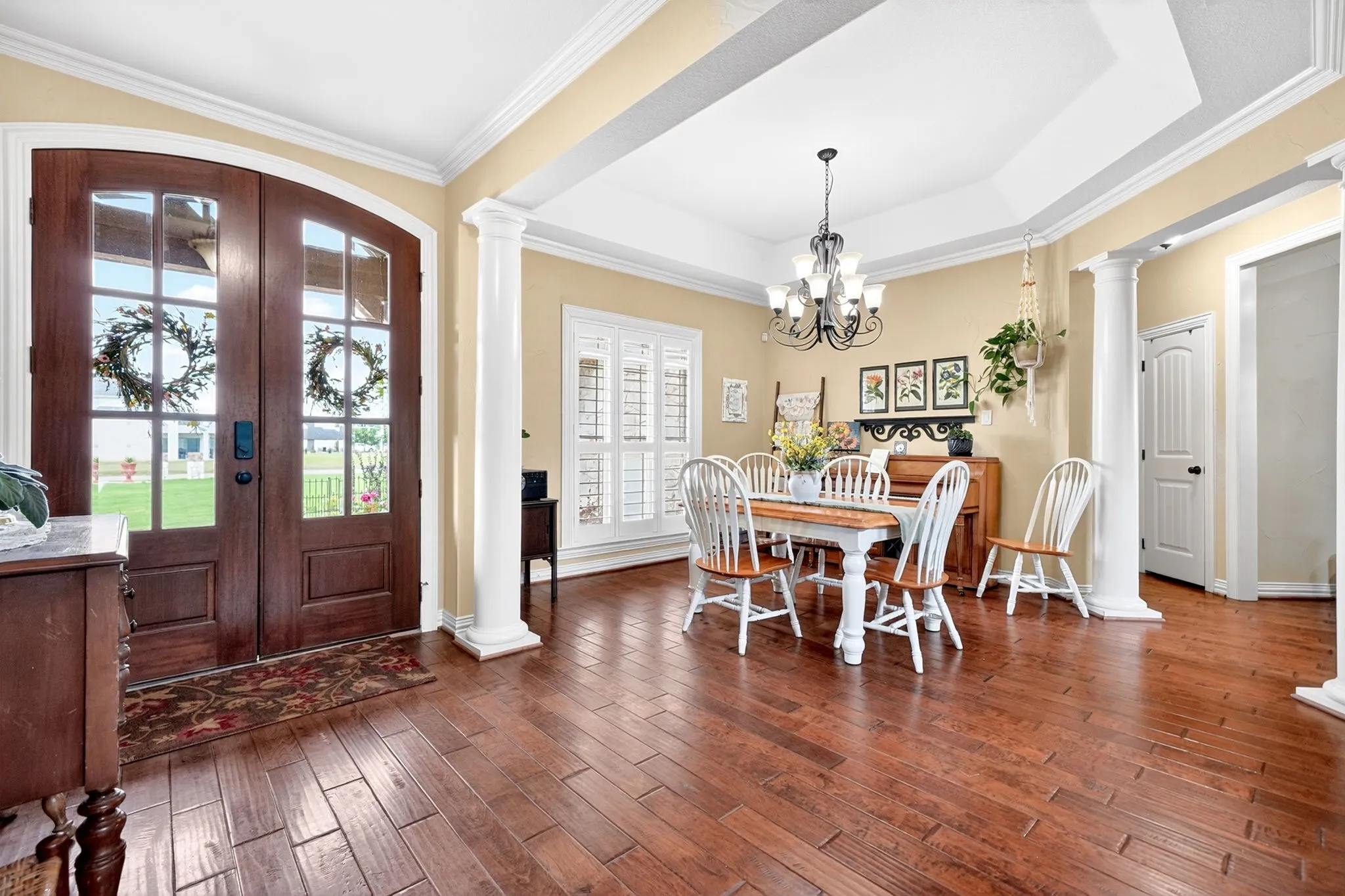 Expansive entry with wood-finish flooring, double arched glass-panel doors, and decorative columns