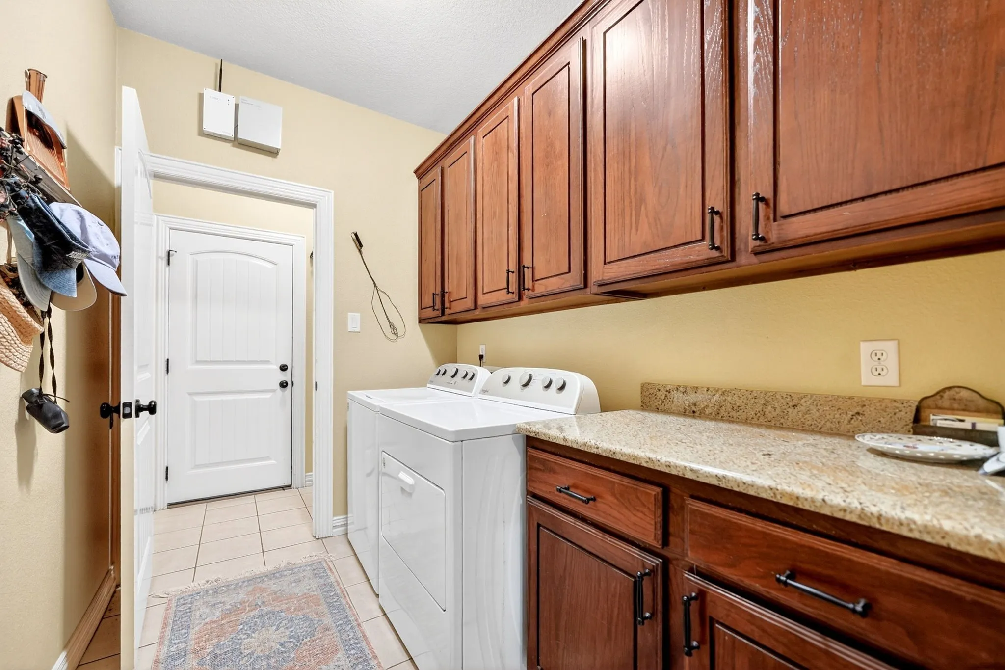 Laundry room featuring rich wood cabinetry, a light granite countertop, and tiled flooring