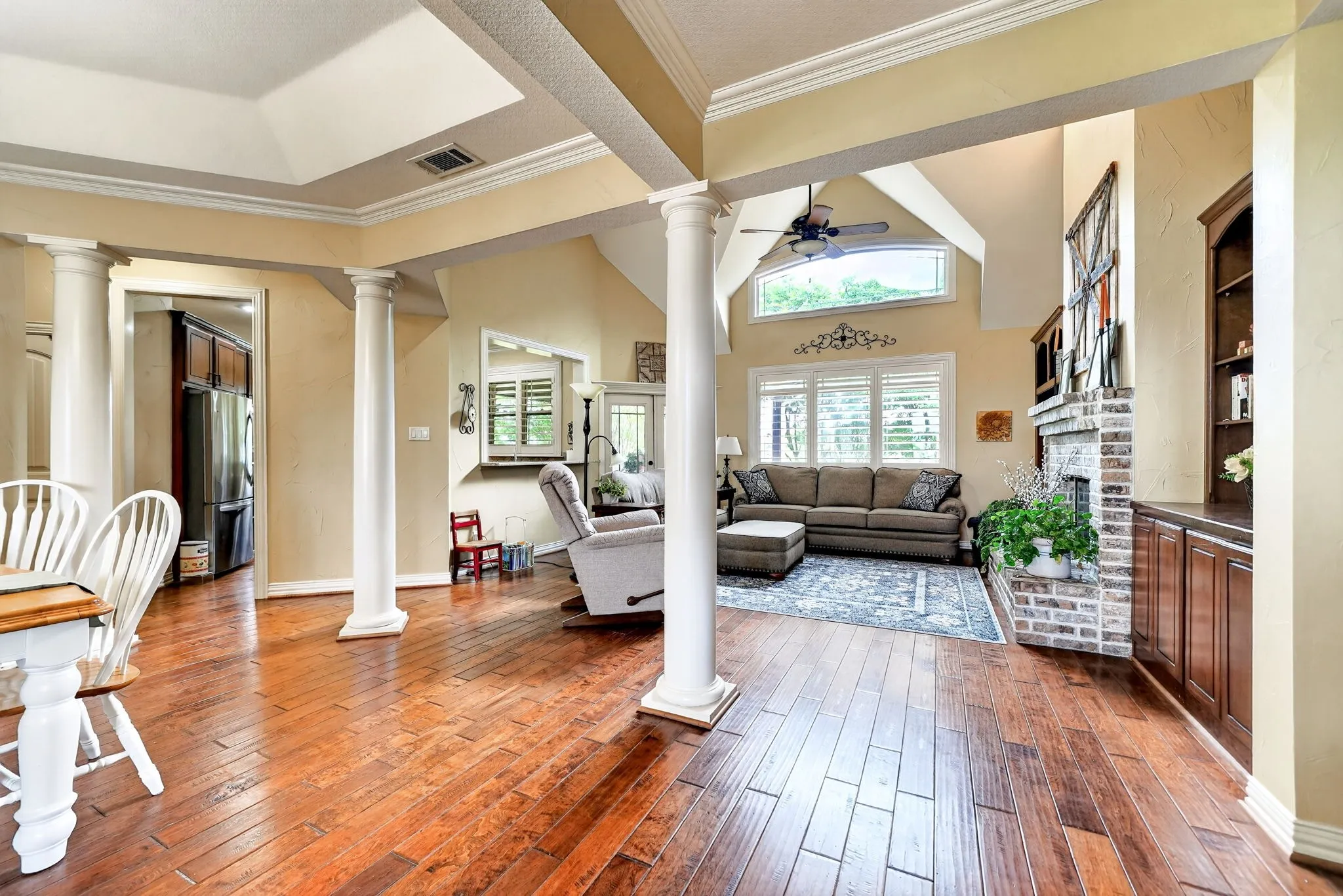 Spacious living area featuring rich wood-finish flooring, vaulted ceilings, and a brick-surround fireplace