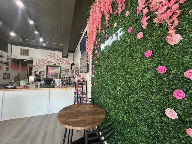 115 E Wall Street is Boba Tea Cafe.  Focal wall featuring a green foliage backdrop with pink floral accents and a neon sign