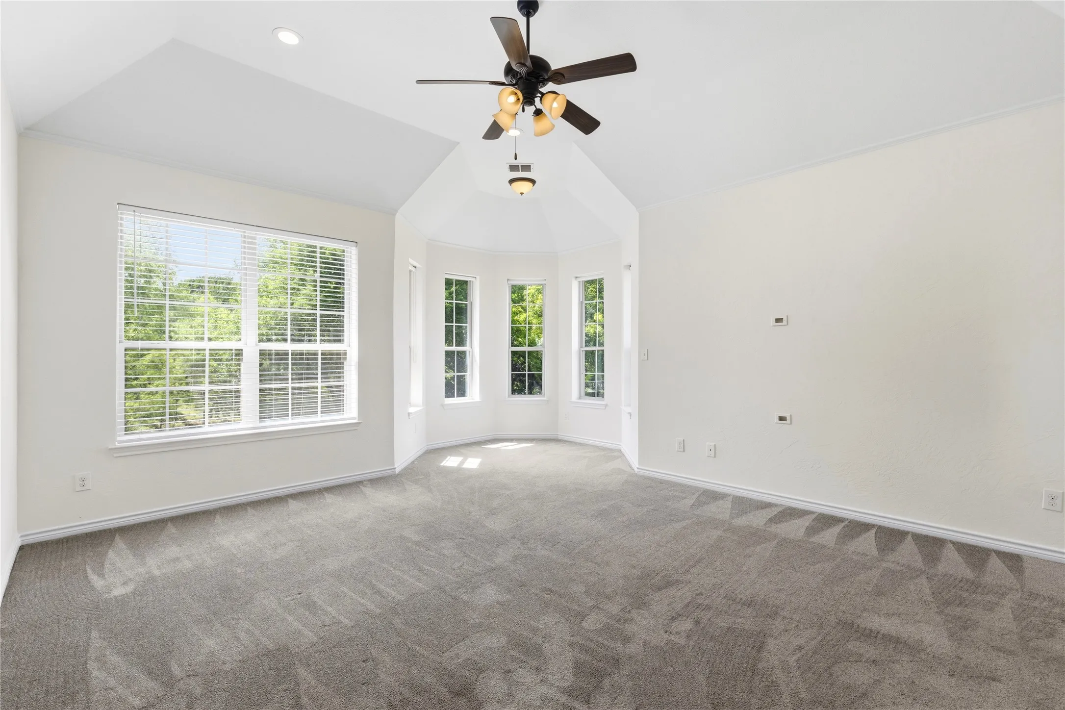 Spacious room featuring vaulted ceilings, a prominent bay window area, and a large window with white blinds