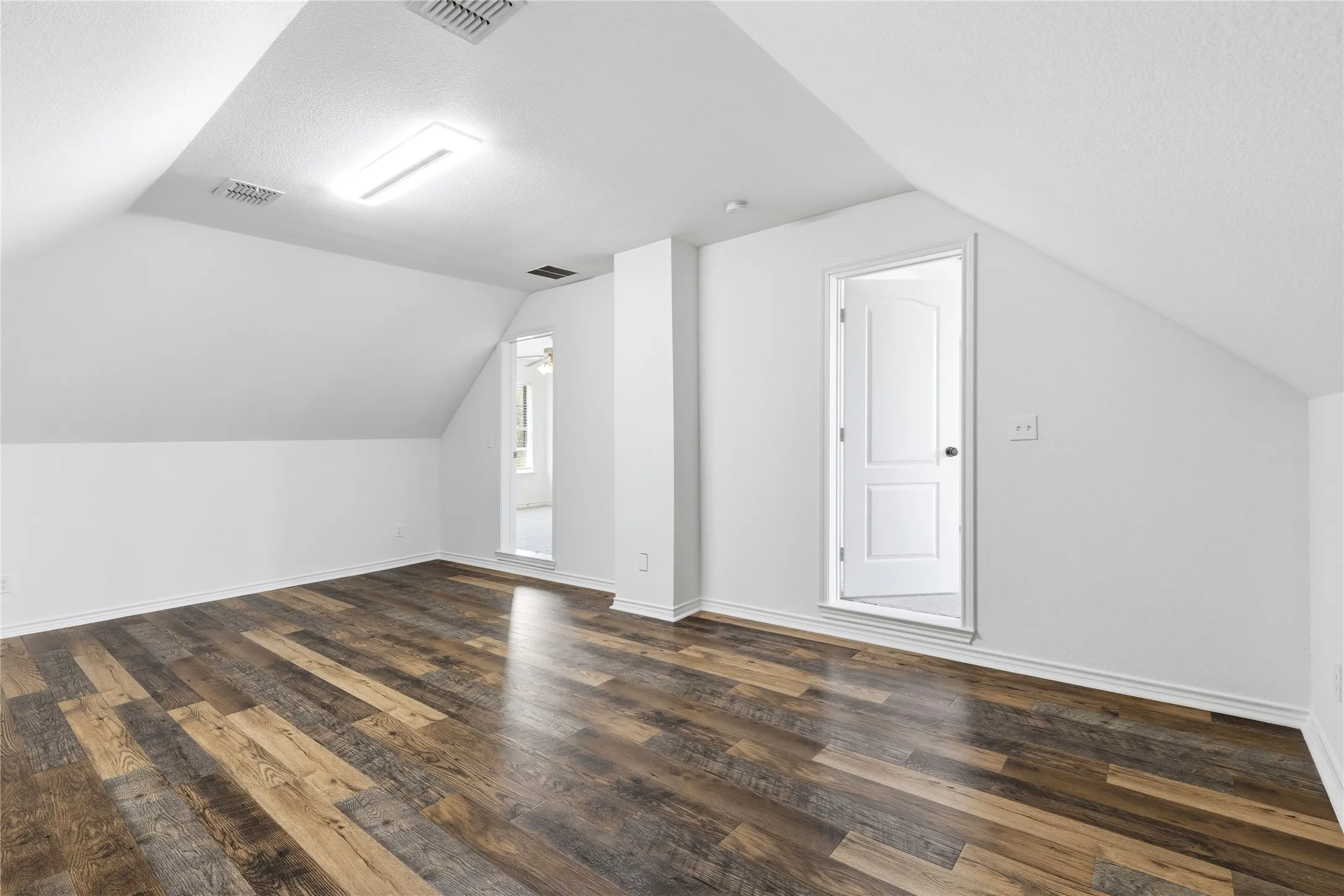 Spacious room featuring sloped ceilings, wood-finish flooring, recessed lighting, and a white paneled door