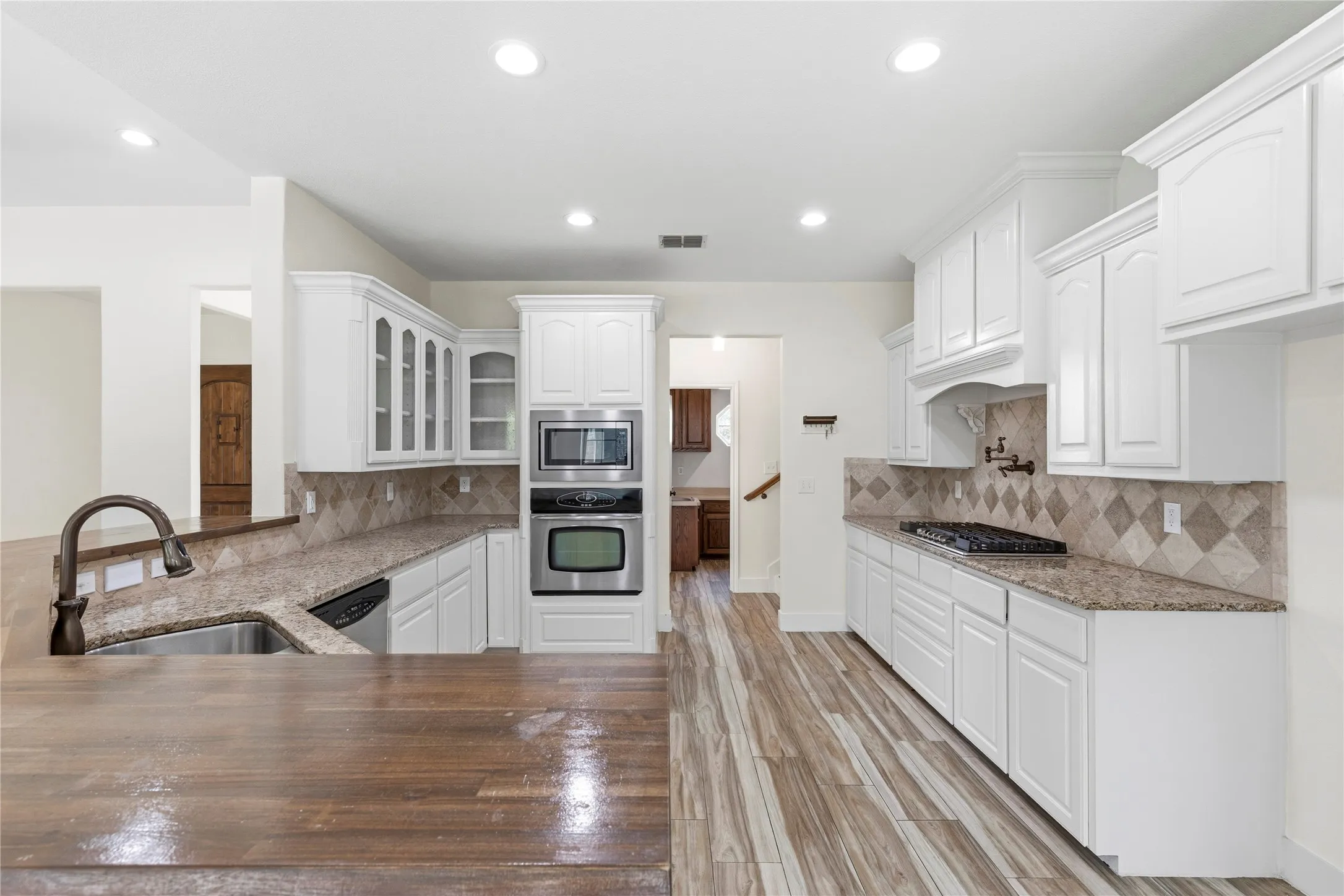 Open-concept kitchen featuring white shaker cabinetry, stainless steel appliances, granite countertops, a diamond-patterned tile backsplash, and wood-finish flooring