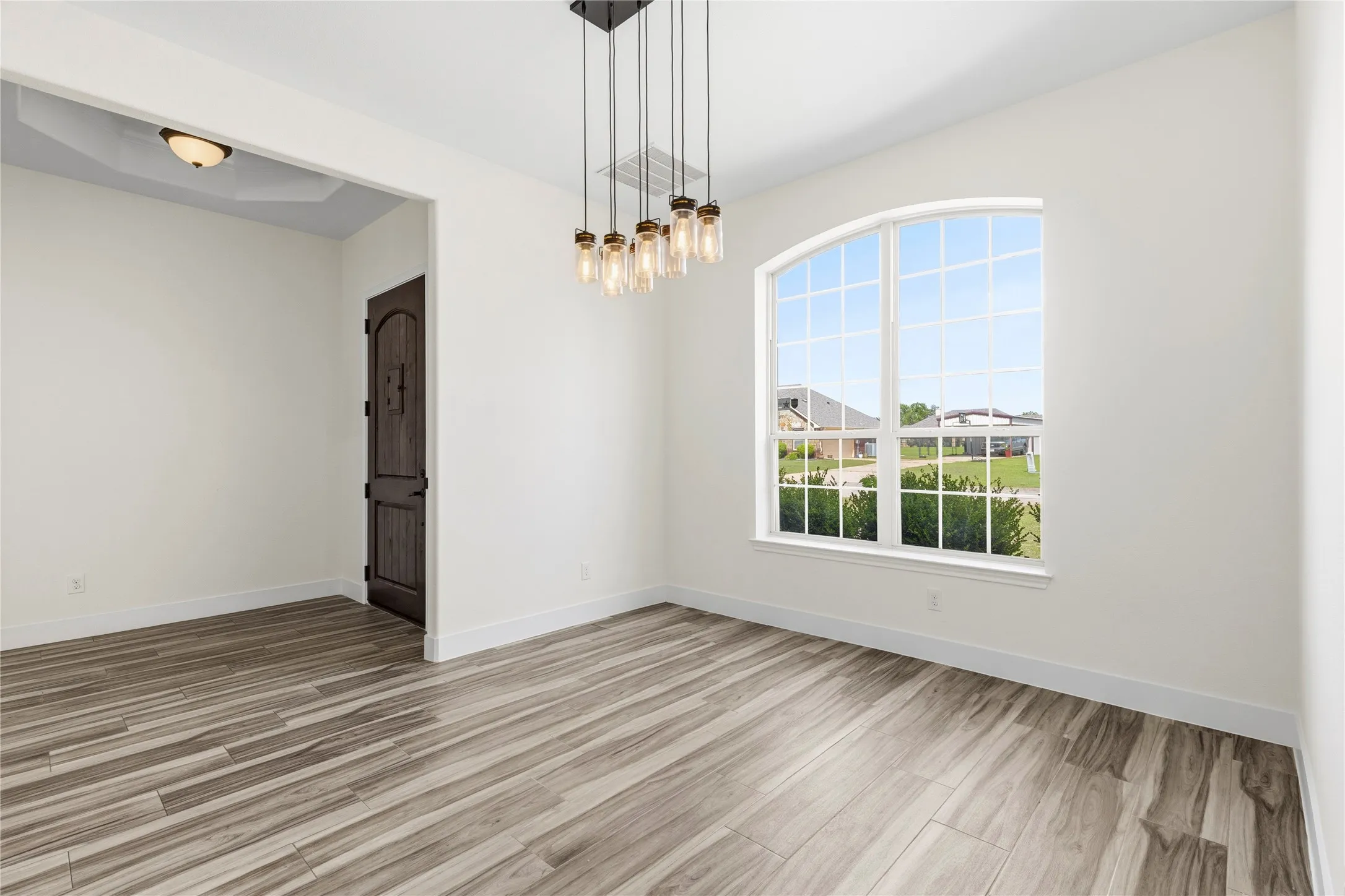 Spacious room featuring wood-finish flooring, a contemporary multi-bulb linear chandelier, and an arched window with grid panes